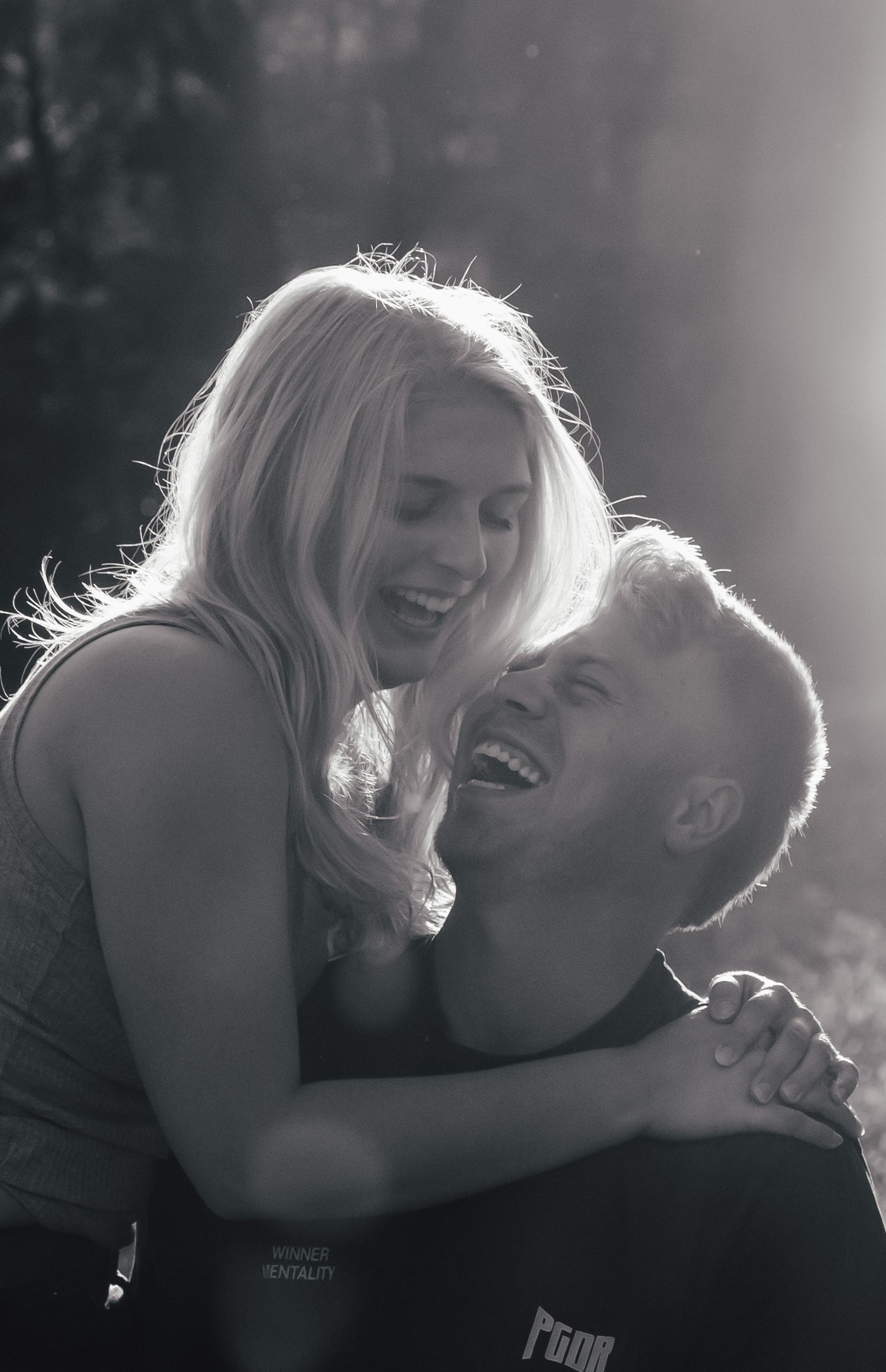 Two people share an intimate laughing moment in dramatic black and white lighting.