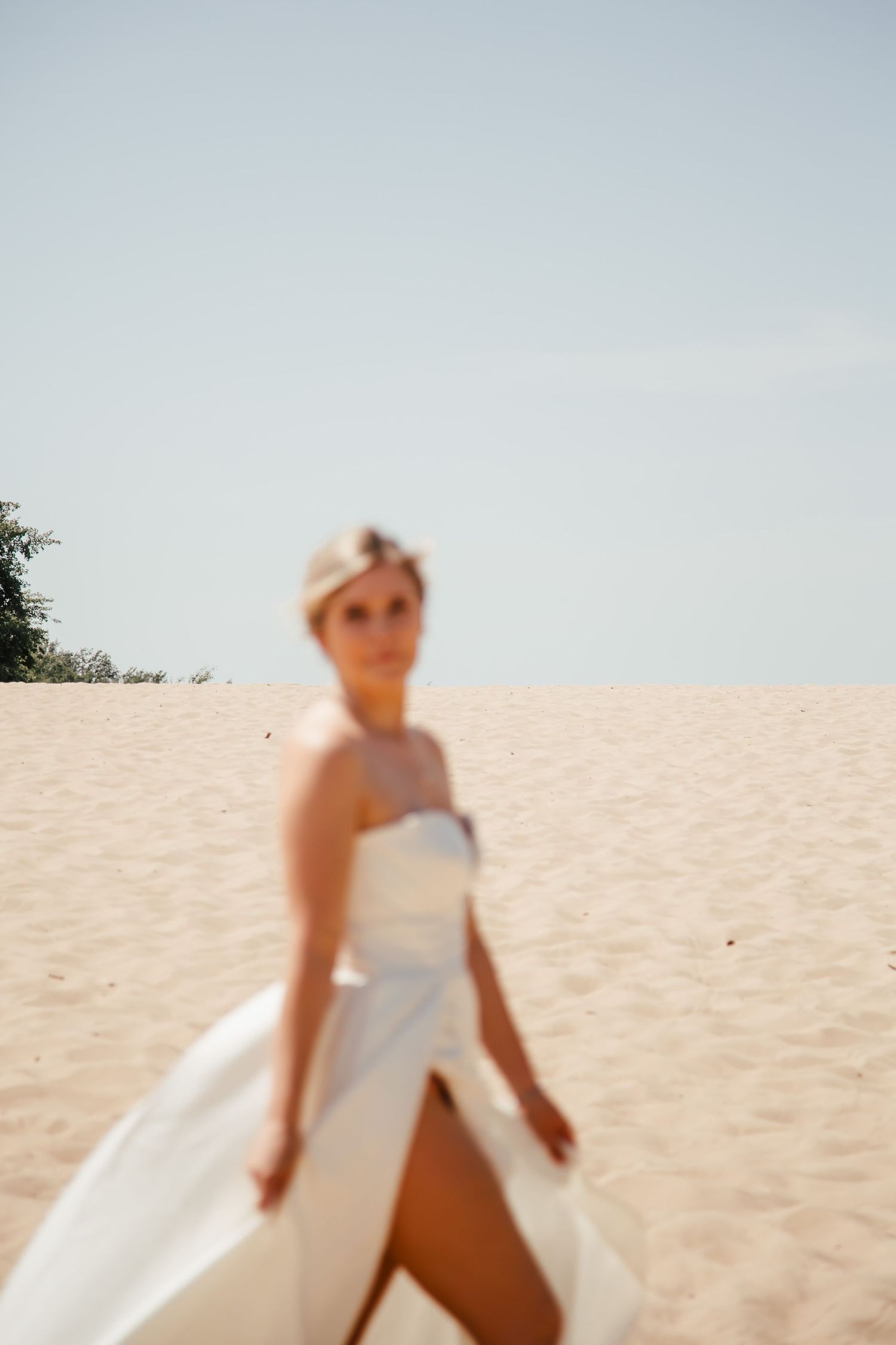 Person in white wedding dress twirling on sandy beach under bright sky.