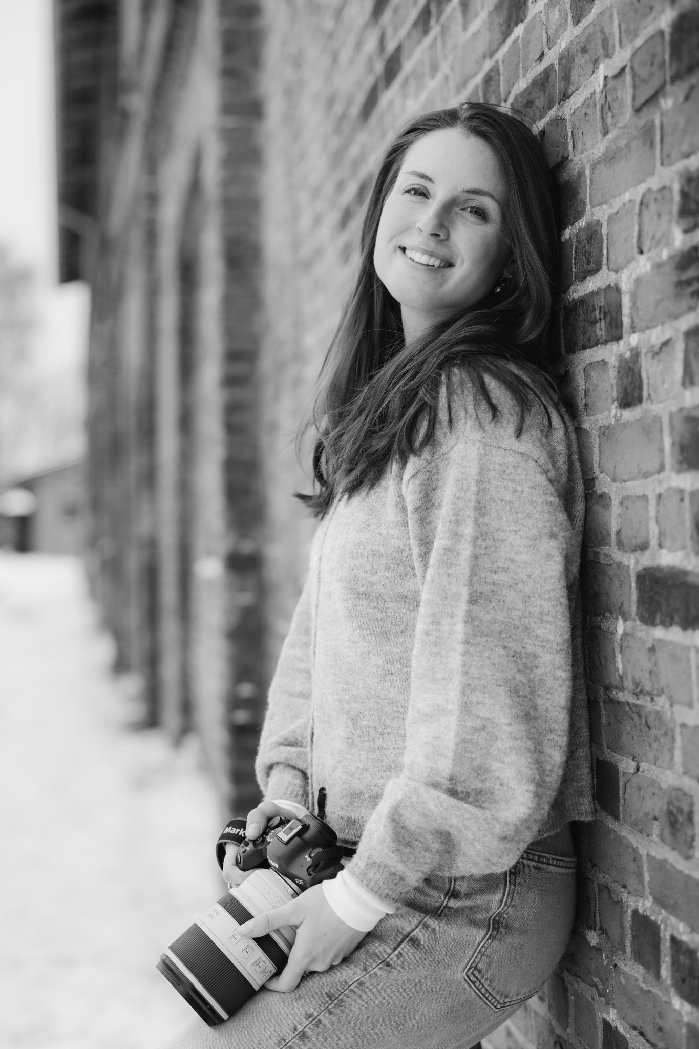 A casual portrait session against a brick wall featuring a cozy sweater and natural lighting.