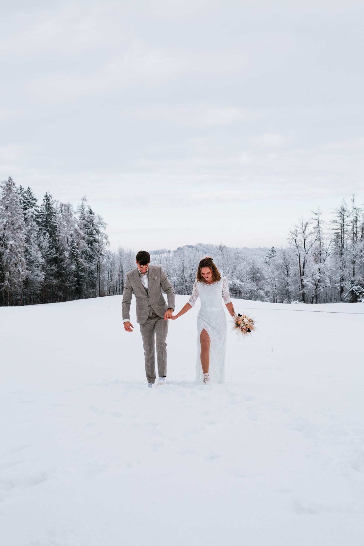 Winter wonderland wedding scene with couple walking through snow-covered landscape.