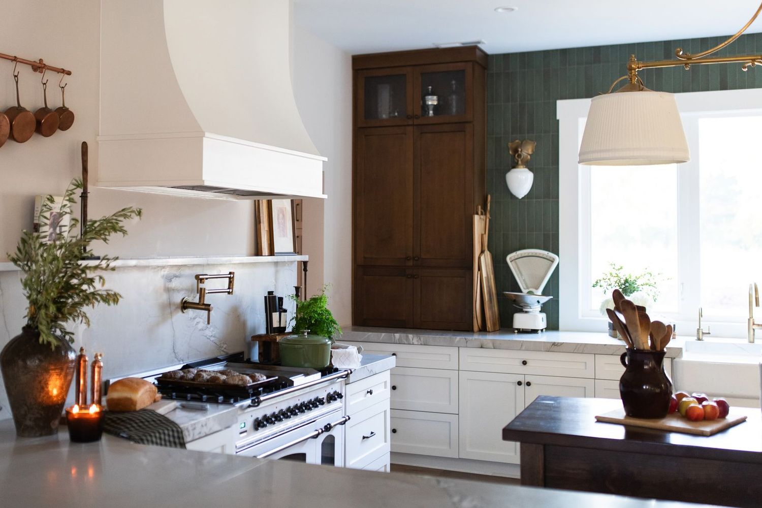 Elegant kitchen with white cabinets, dark wood armoire, professional range, pendant light, and green wallpaper accents.