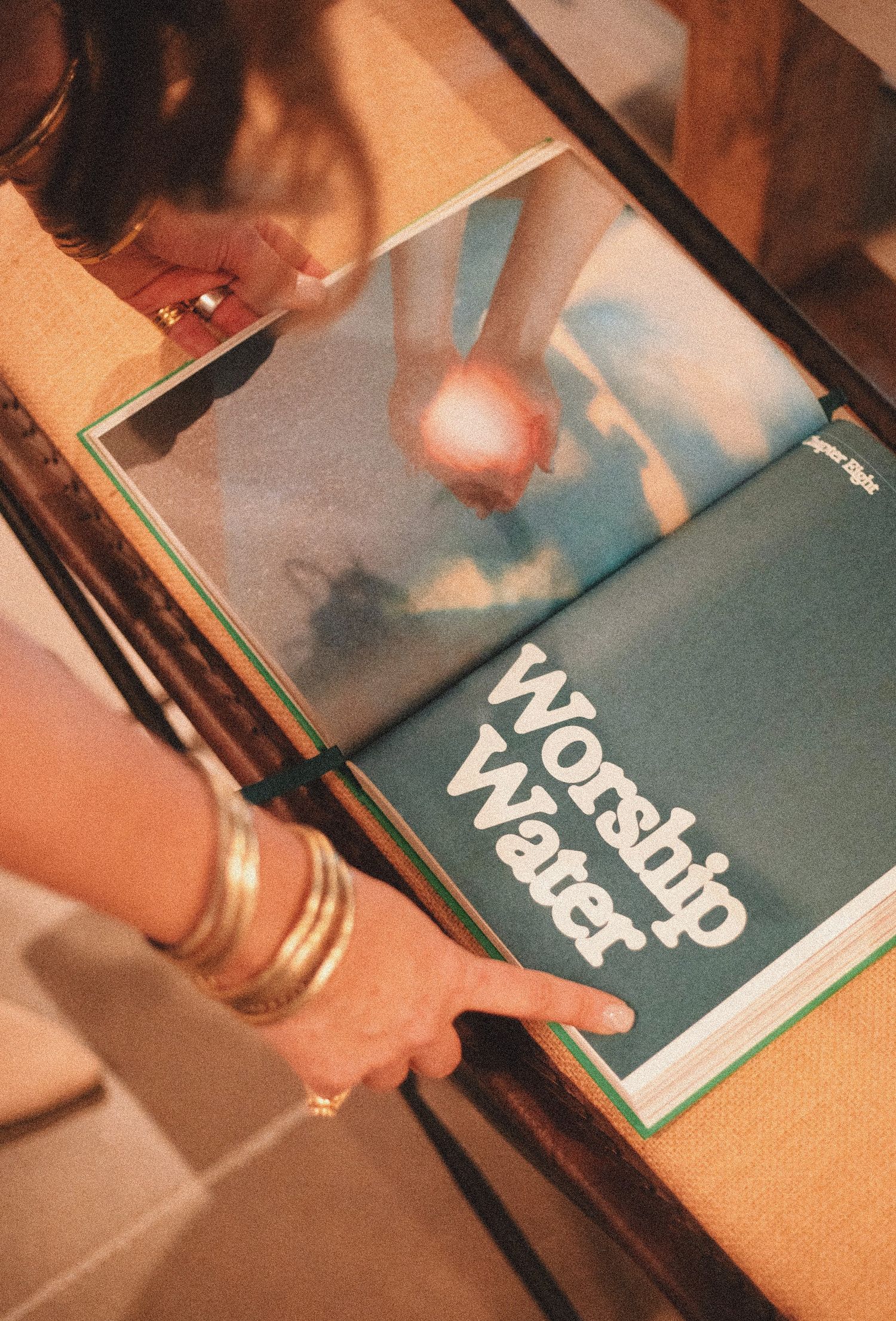 Person holding open a book titled Worship Water with a teal cover and ocean photography inside.