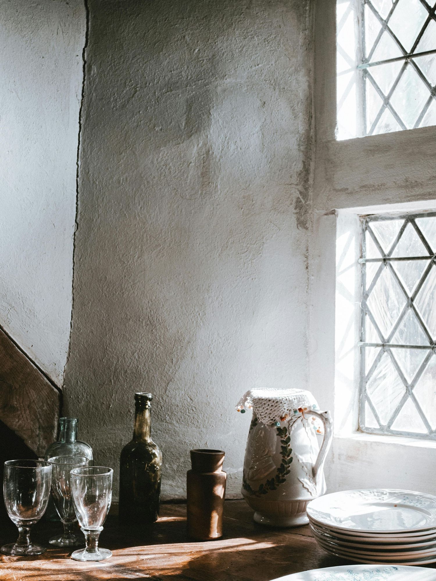 Sunlight streams through diamond-paned windows onto rustic windowsill with vintage glassware.