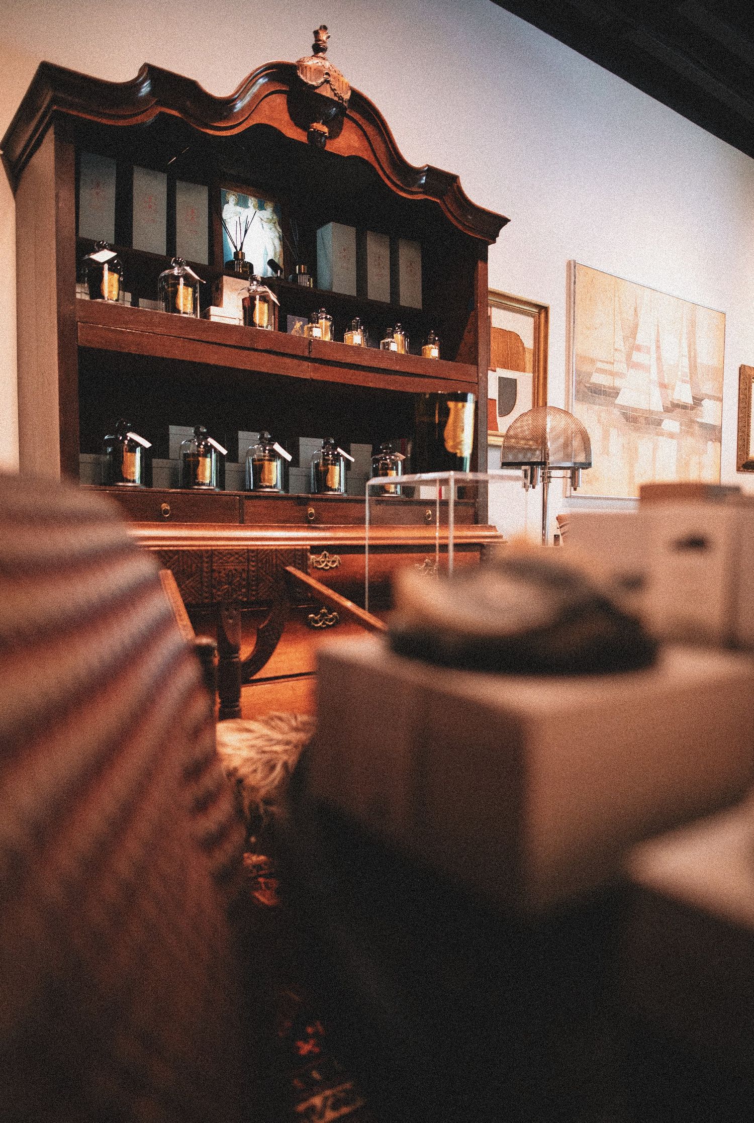 Antique wooden cabinet displaying vintage perfume bottles in a warmly lit, elegant room with artwork on the wall.