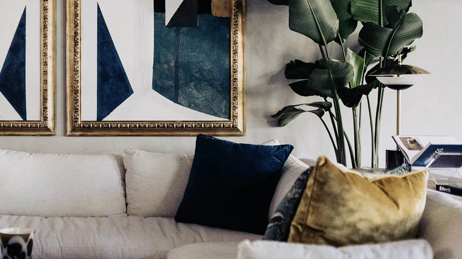 Elegant living space with navy blue accents, gold throw pillows, and lush green plants.