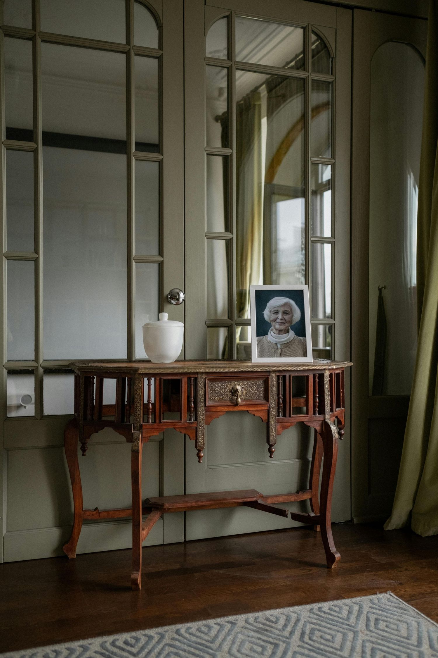 Elegant antique console table with mirror panels and framed artwork in bright interior setting.