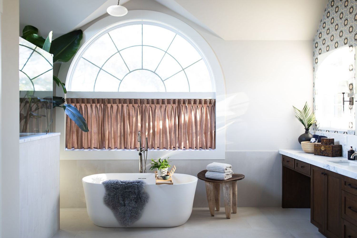 Elegant bathroom with freestanding oval tub, arched window, copper curtains, and dark wood vanity.