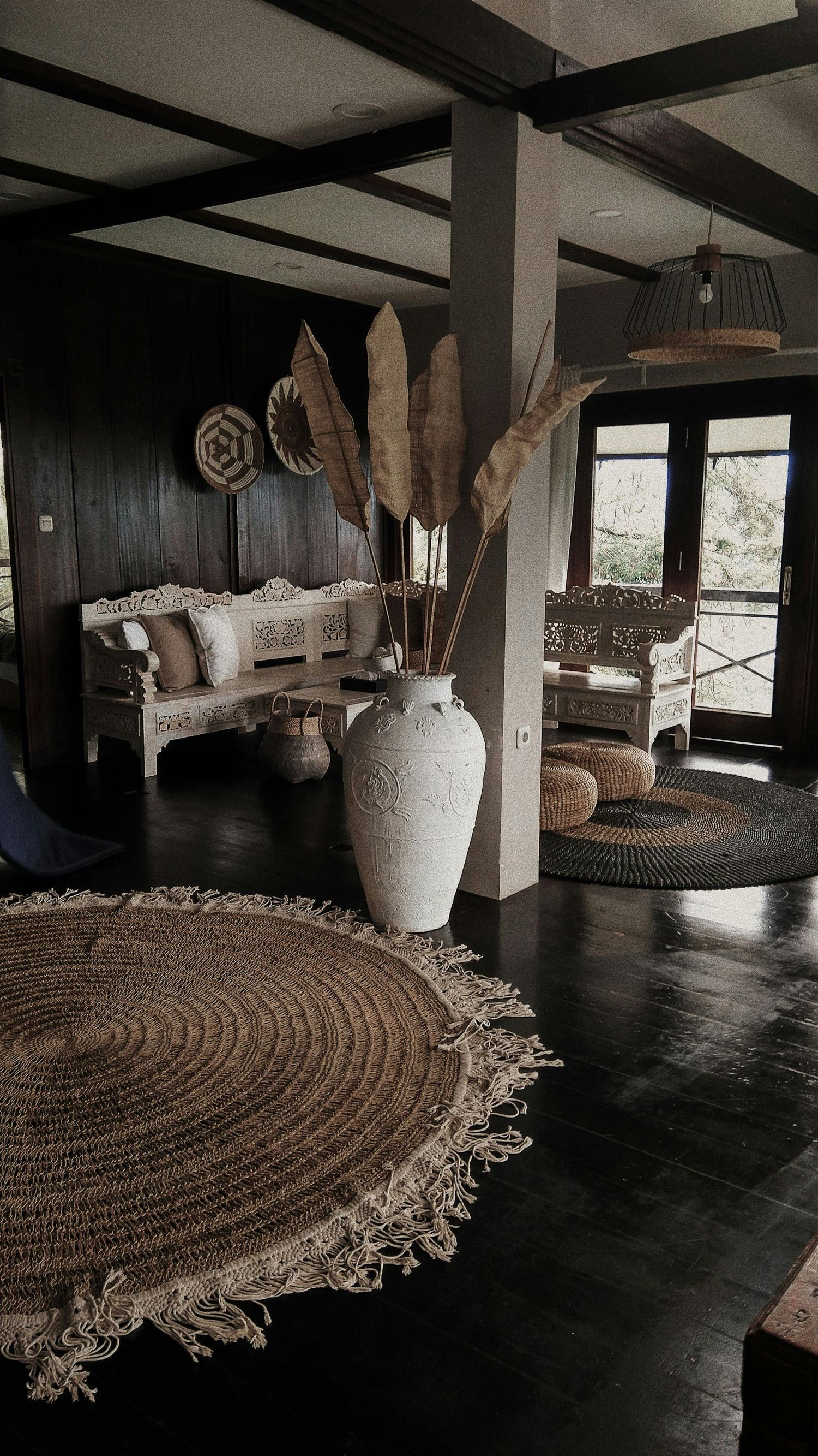 Dark room with circular jute rug and white ceramic vessels creating dramatic atmosphere.
