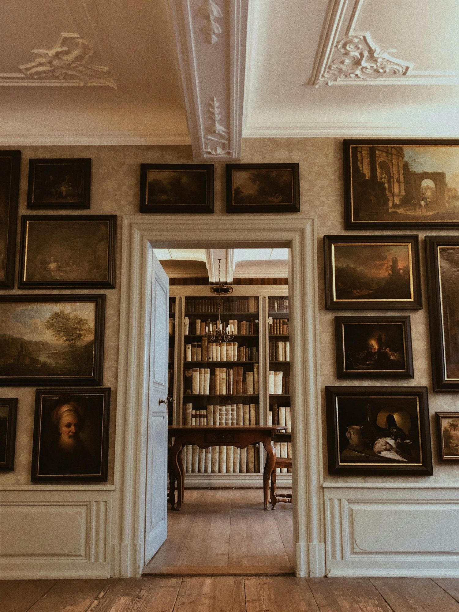 Gallery wall displaying vintage paintings and bookshelves in an elegant room with ornate moldings.