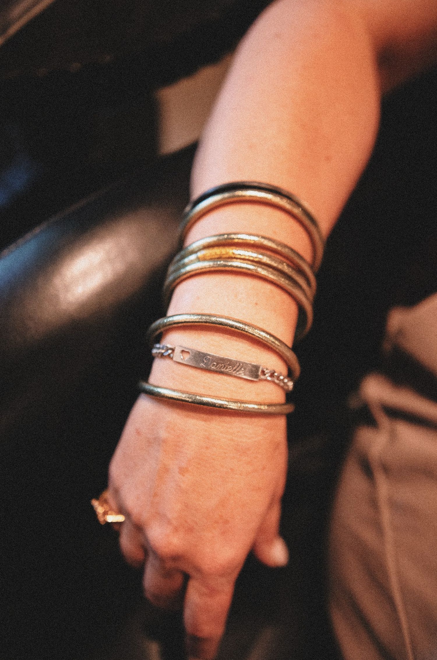 A wrist adorned with multiple stacked silver and gold bangle bracelets, including an engraved bar bracelet.