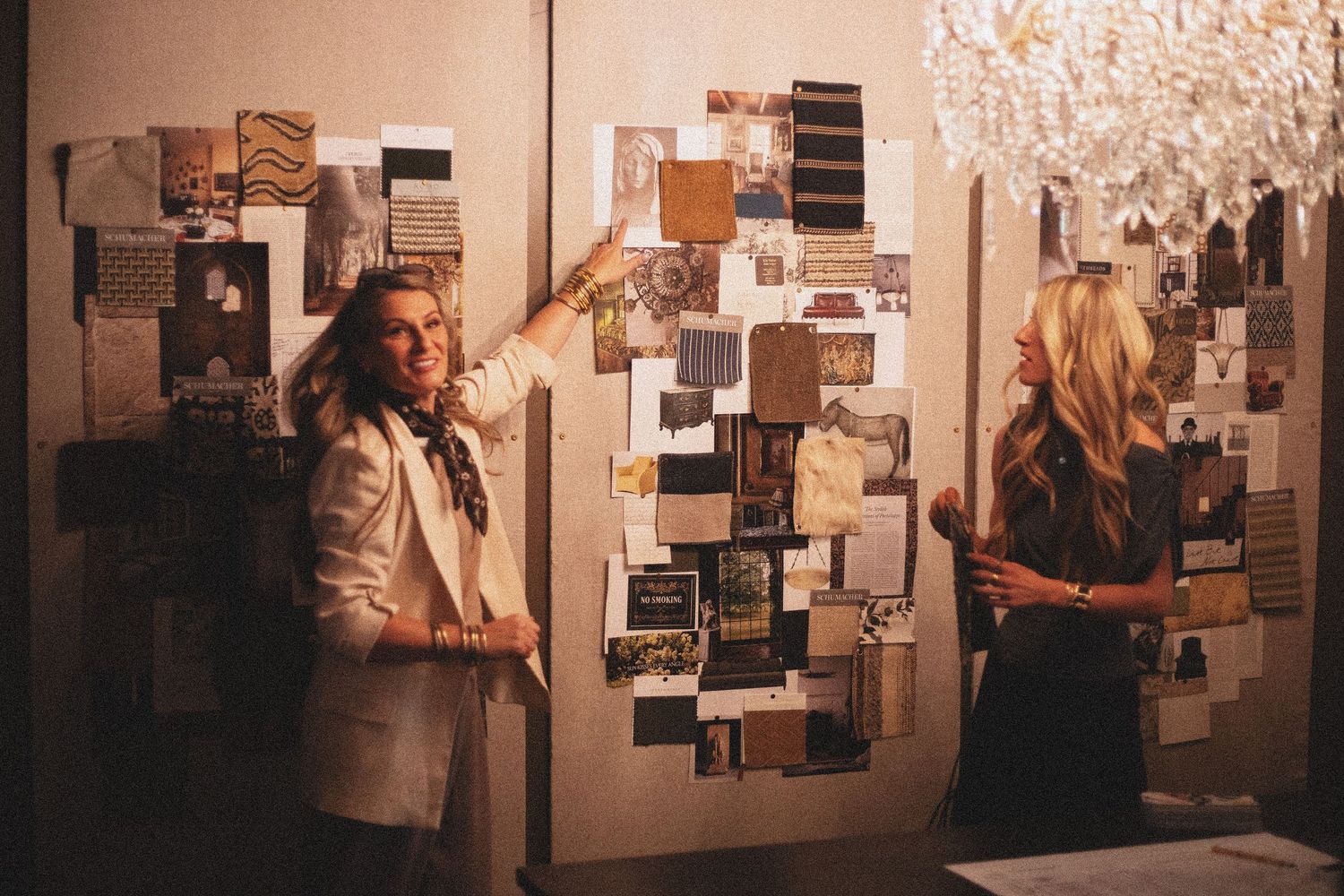 Two women reviewing an interior design mood board with fabric swatches and samples on a wall.