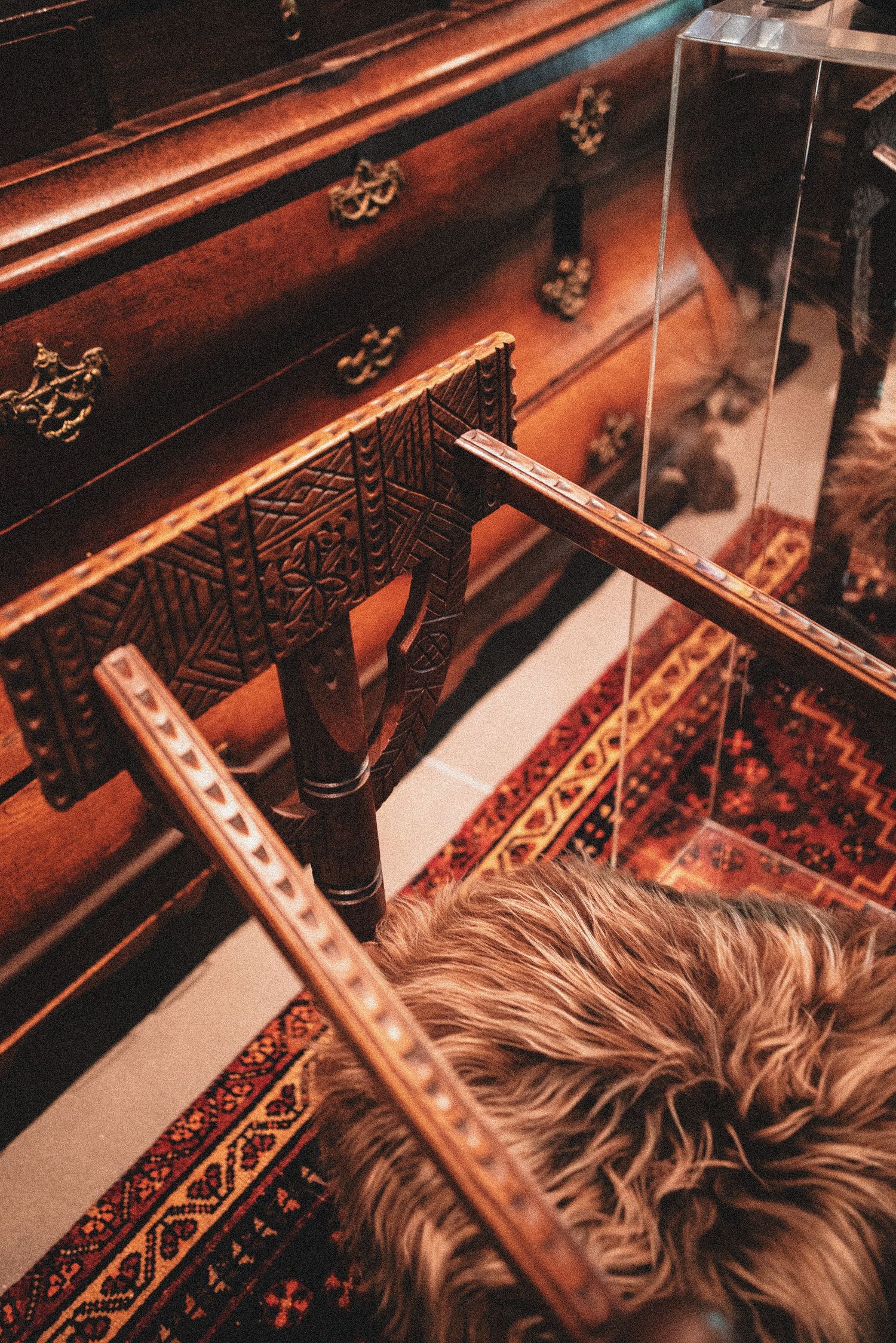 Antique wooden dresser with brass handles beside an ornate carved chair on a red patterned rug.