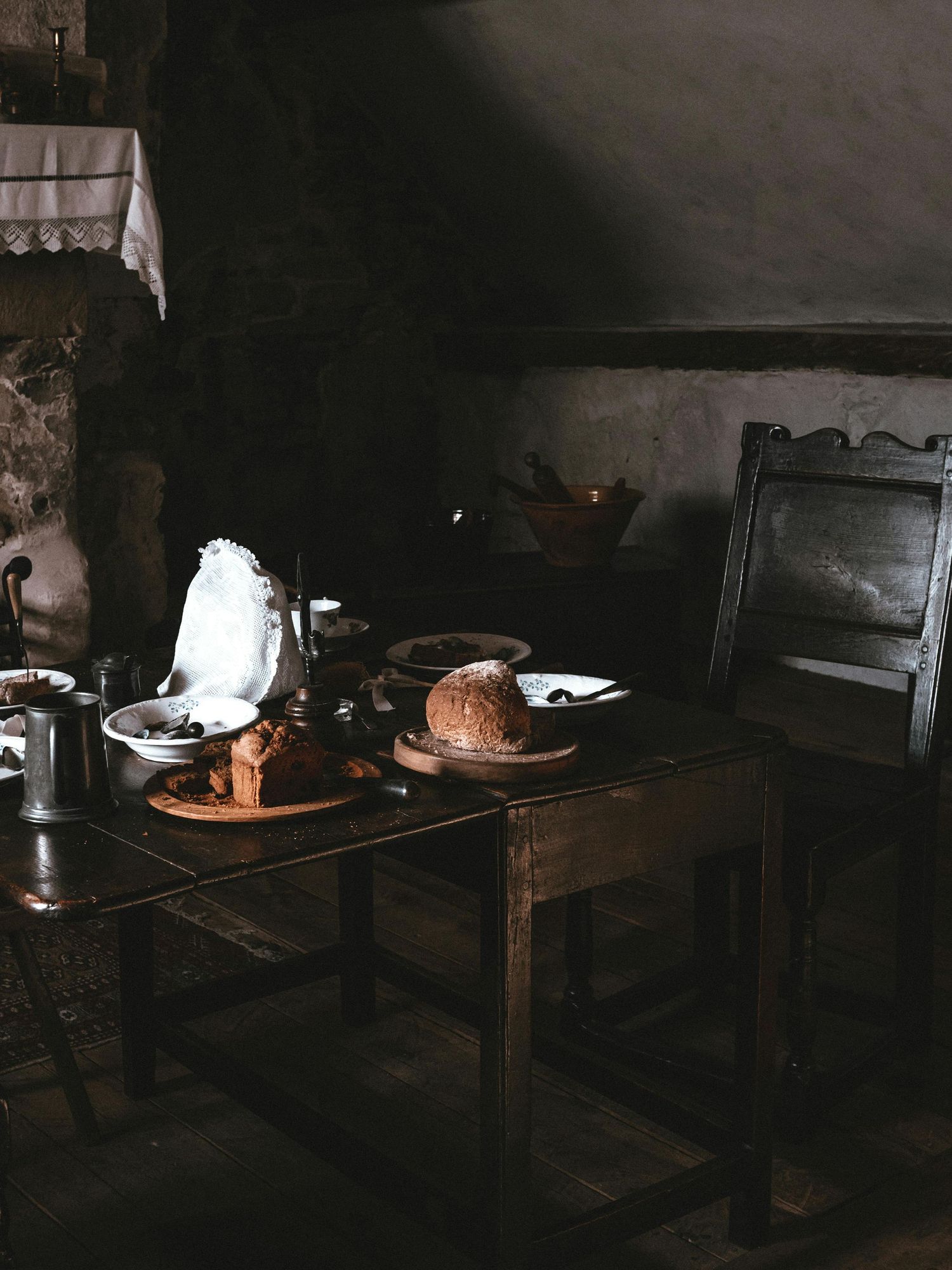 Dark moody interior scene with antique furniture and bread loaf on wooden table.