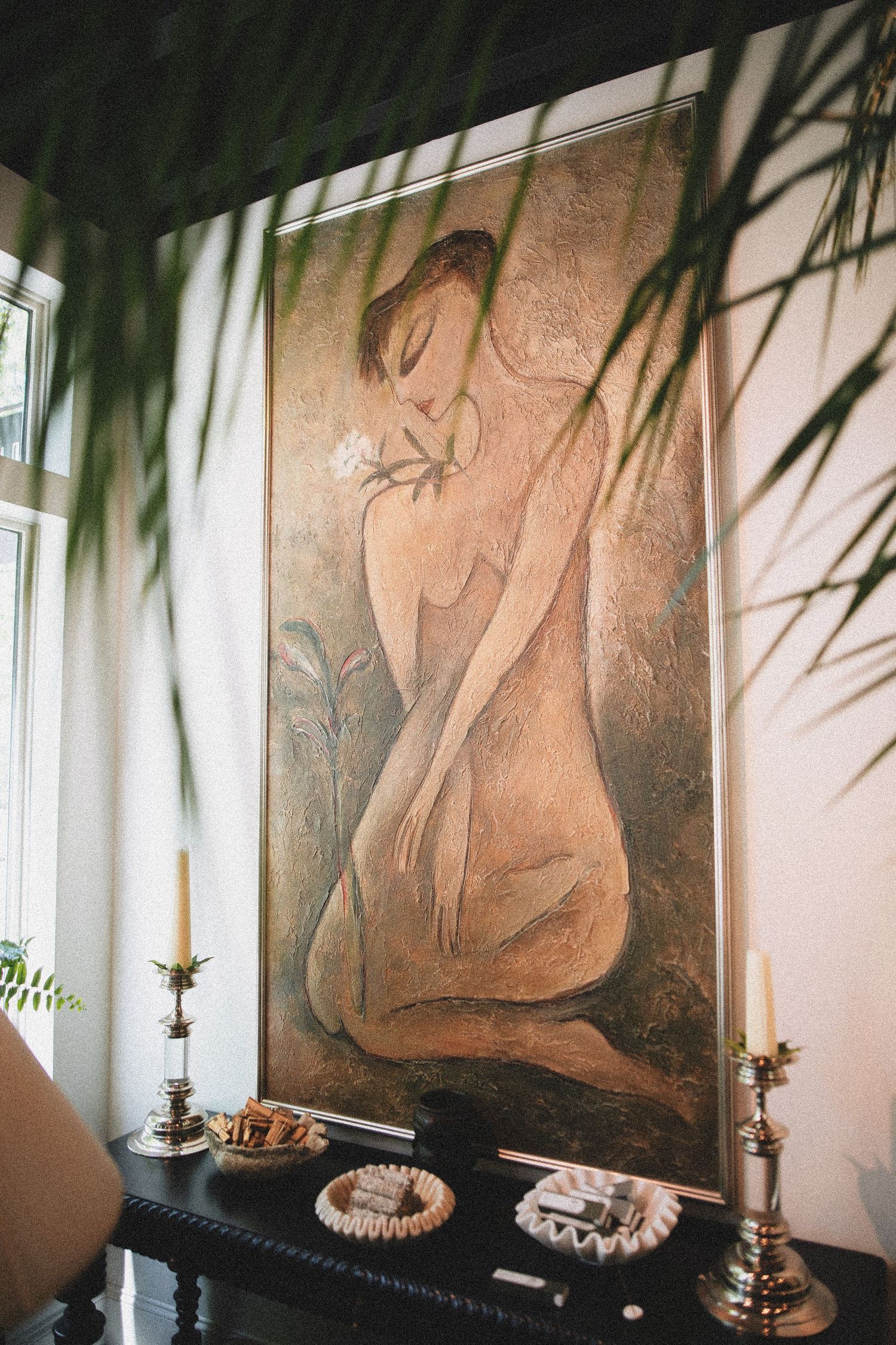 Large figurative painting of a nude woman with a flower above a console table with brass candlesticks.