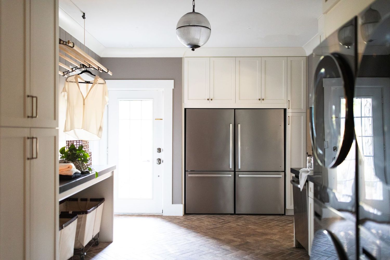 Bright kitchen with cream cabinets, stainless steel French door refrigerator, herringbone tile floor, and pendant light.