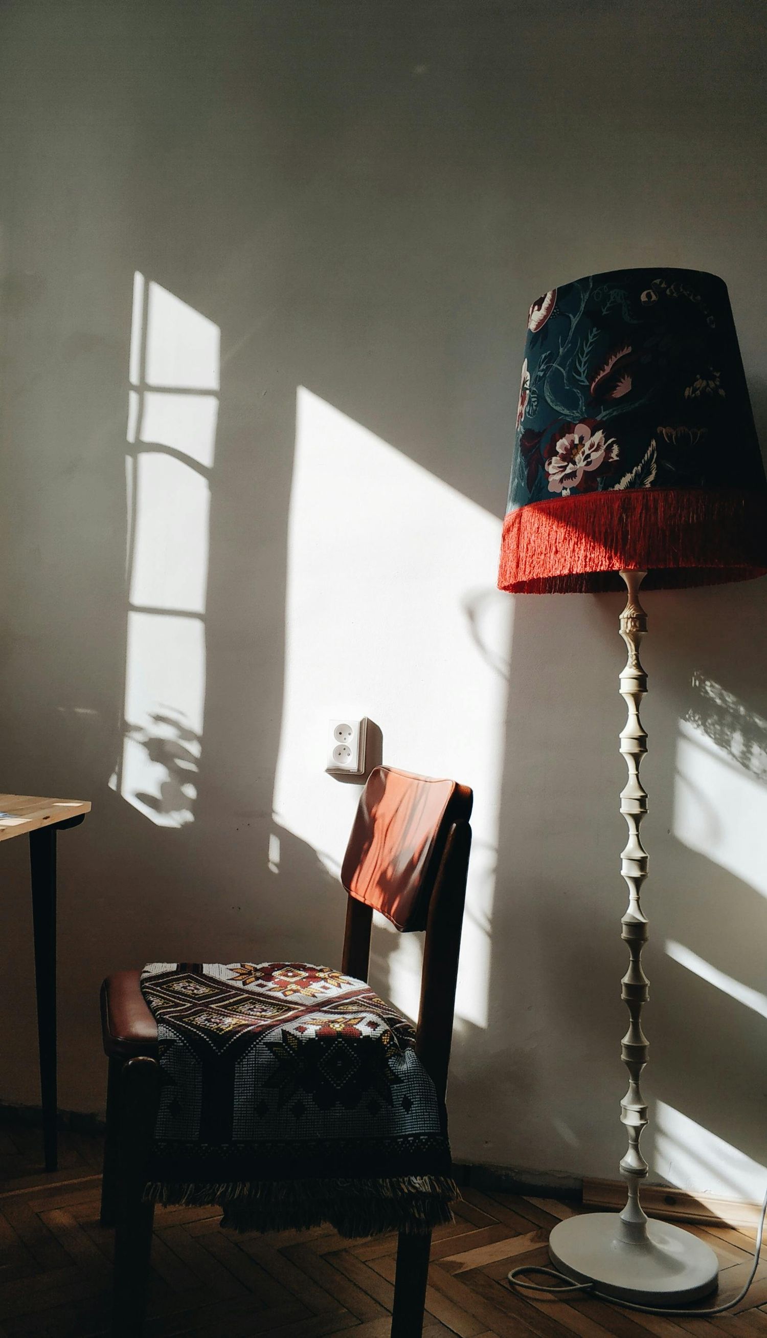 Decorative floor lamp with blue and red shade casting dramatic window shadows on wall.