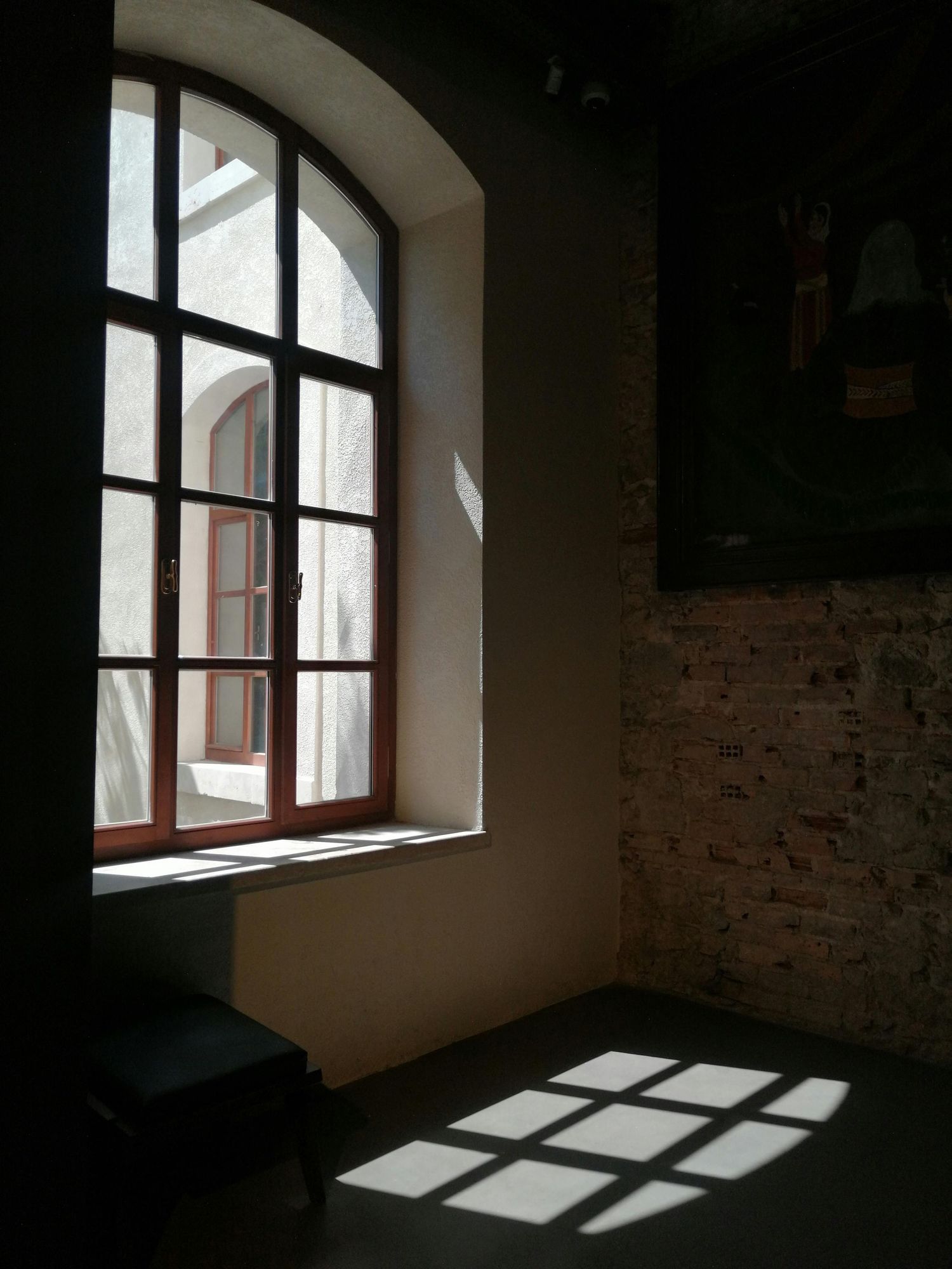 Arched windows casting dramatic shadows on interior brick wall.