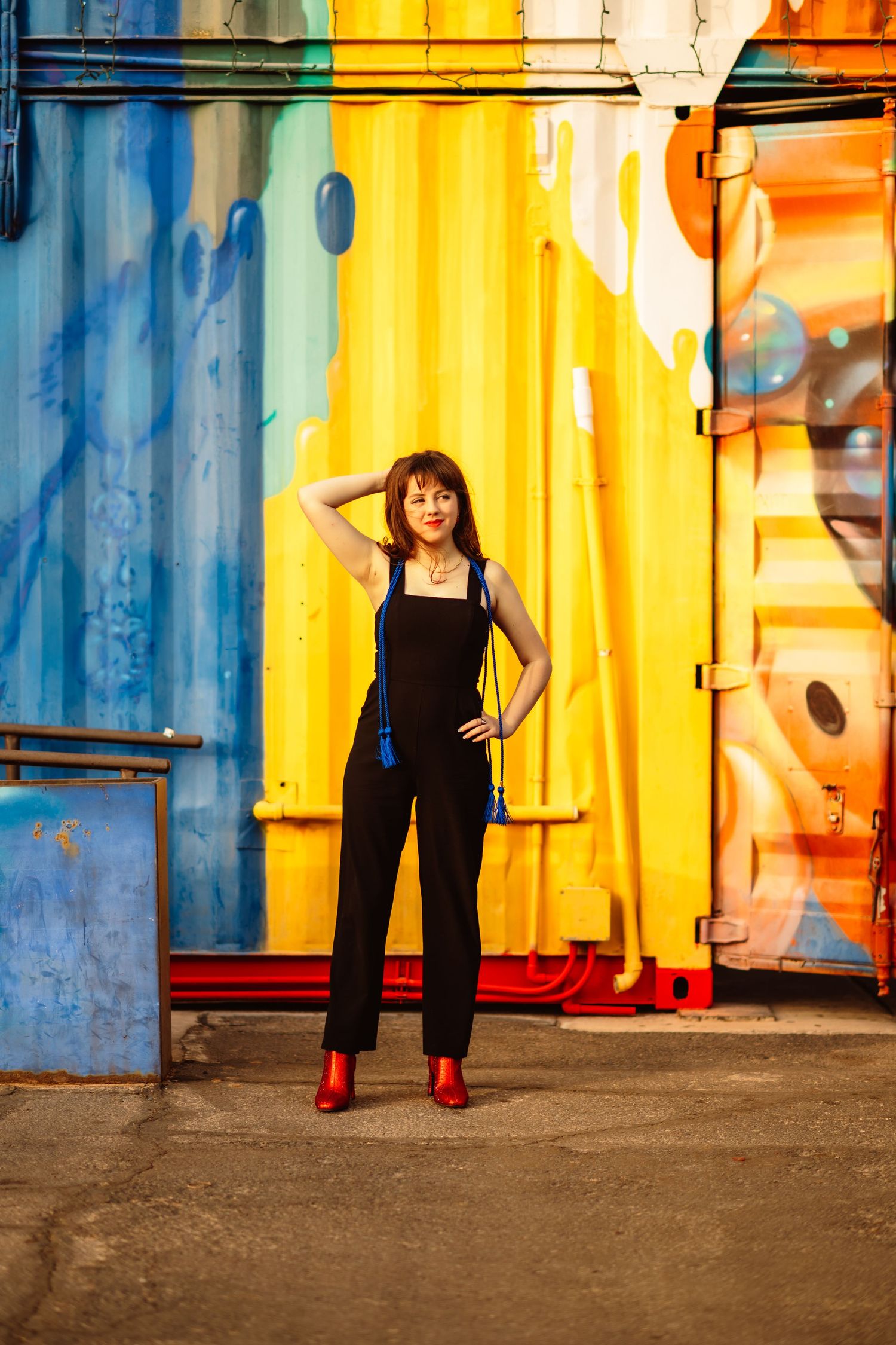 Figure in black outfit against colorful shipping container wall with red shoes.