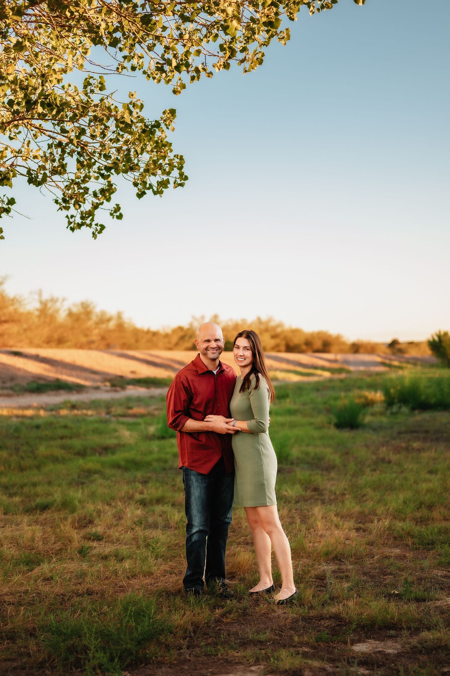 A couple shares an intimate moment in a field during golden hour with trees in the background.