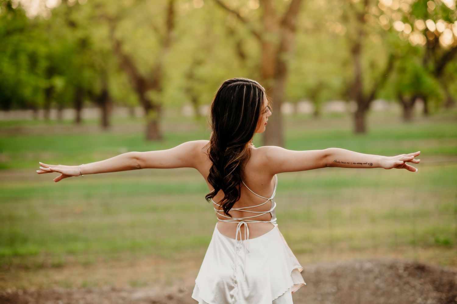 A person in a white dress twirls gracefully in a sunlit outdoor garden setting.