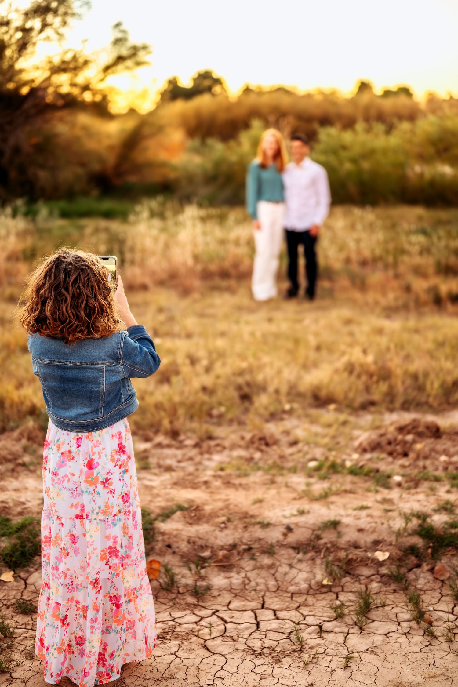 Young photographer captures couple in background during sunset in dried field.