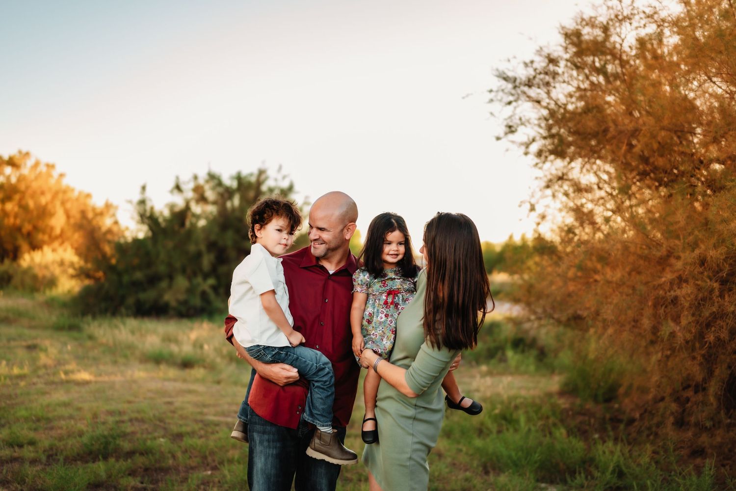 Family portrait session in autumn field with golden sunlight filtering through trees.