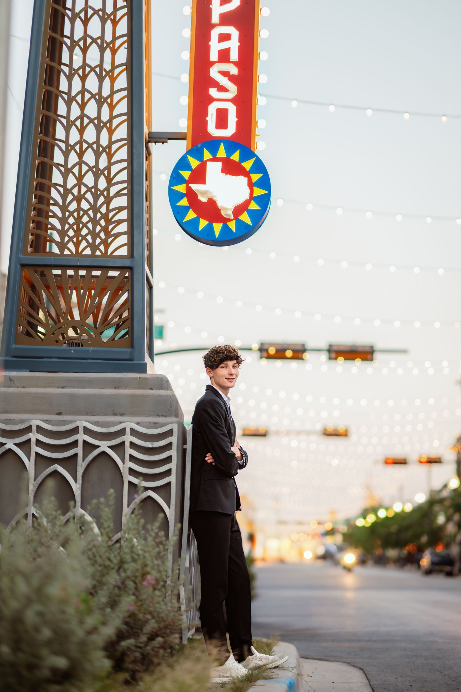 Person in dark formal wear standing near decorative pillars with Texas state signs.