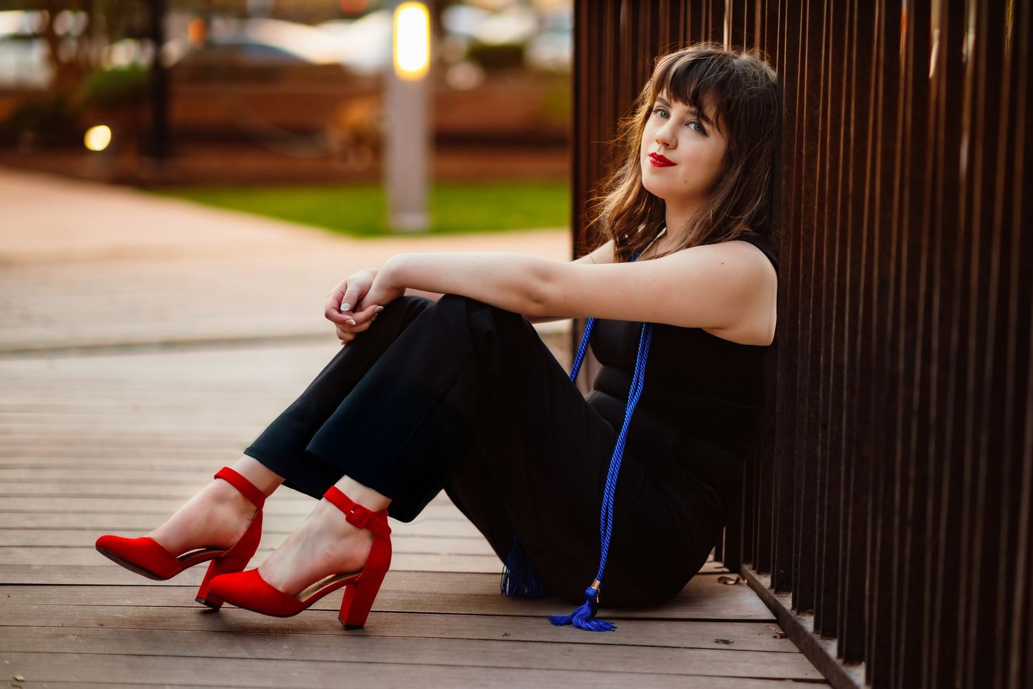 Woman in black outfit with blue accent and red heels sits casually against metal railing.