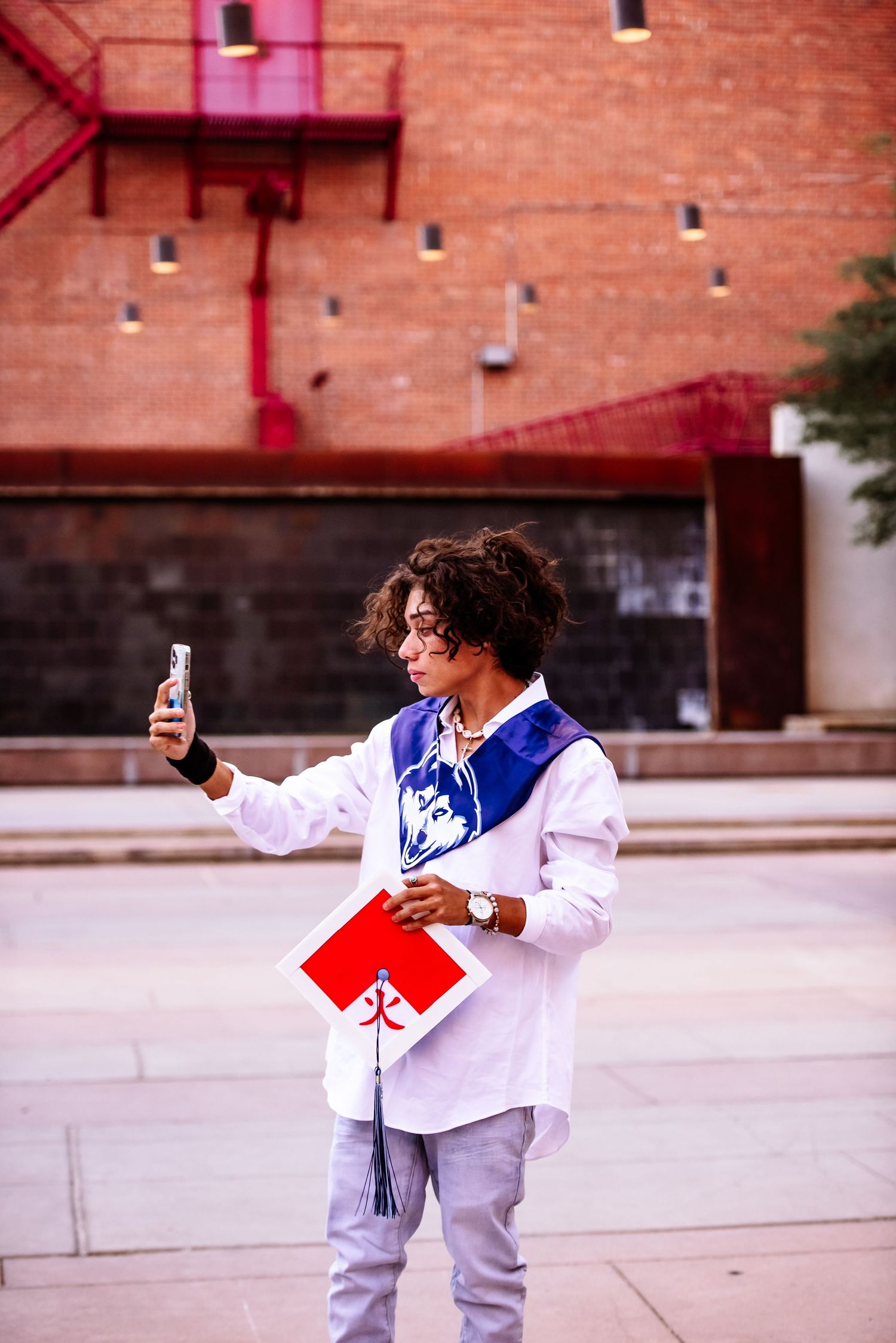 A person in a white outfit strikes dynamic poses while taking selfies in front of a brick building.