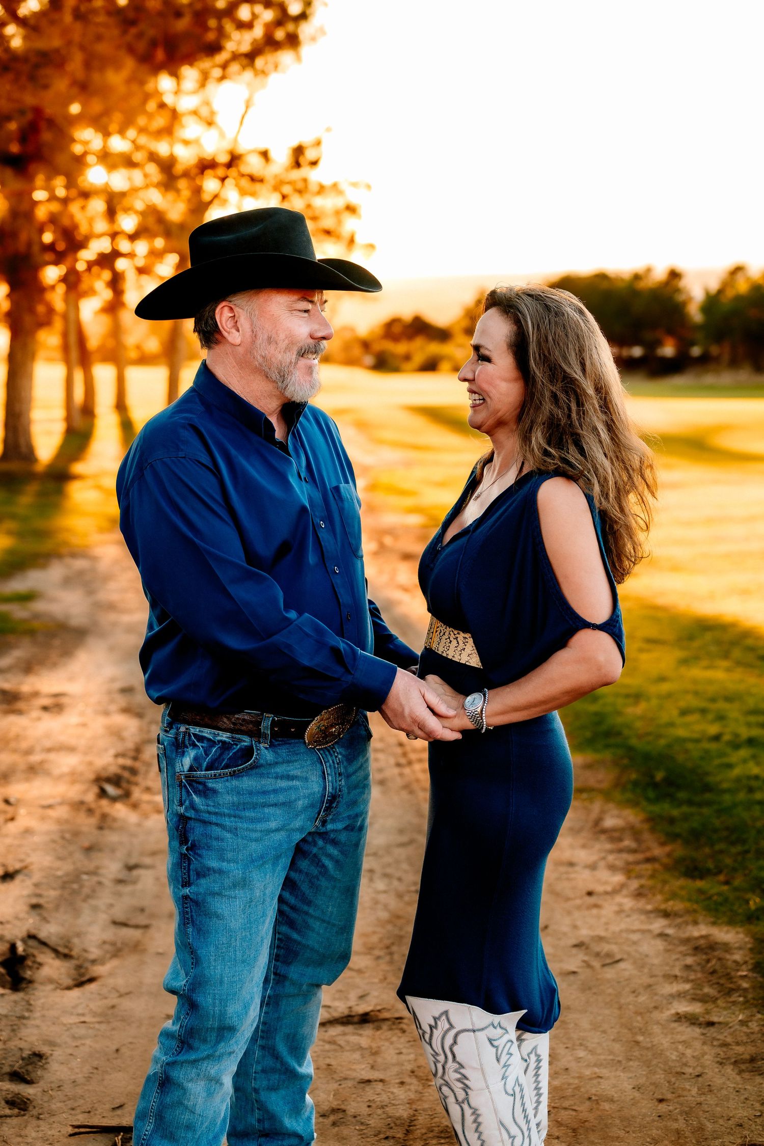 A couple in western attire dances together on a dirt path at sunset.