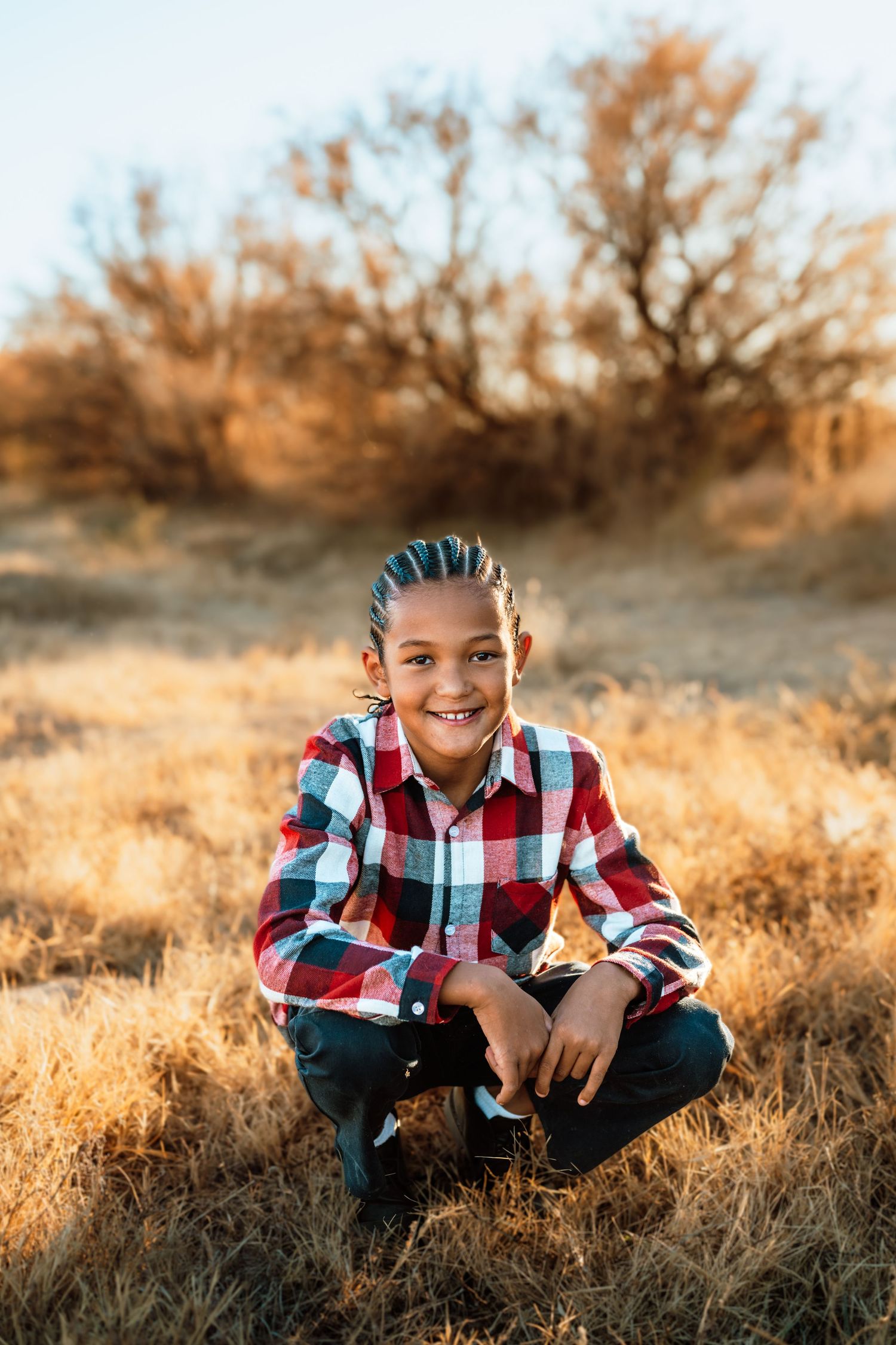 Child sits in golden grass during sunset wearing plaid shirt and jeans.