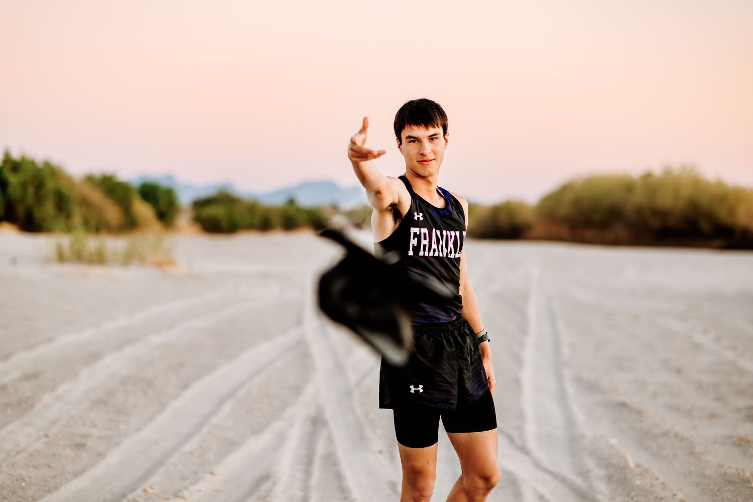 Track athlete poses on dirt road at sunset.