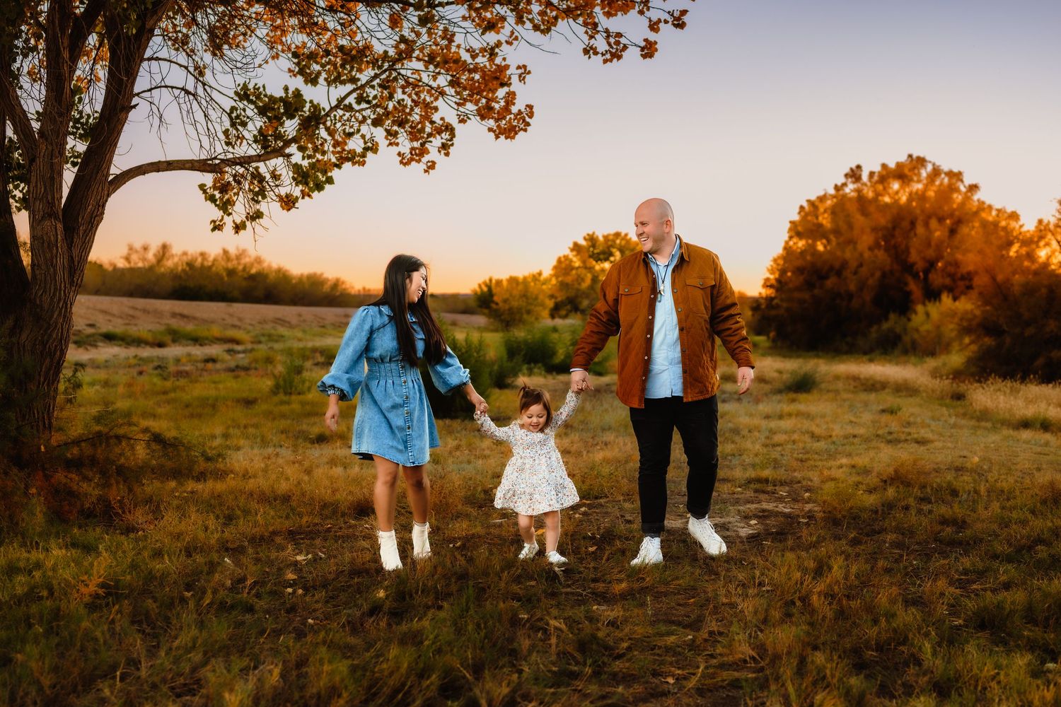 Family walking together through autumn field at sunset with warm lighting.