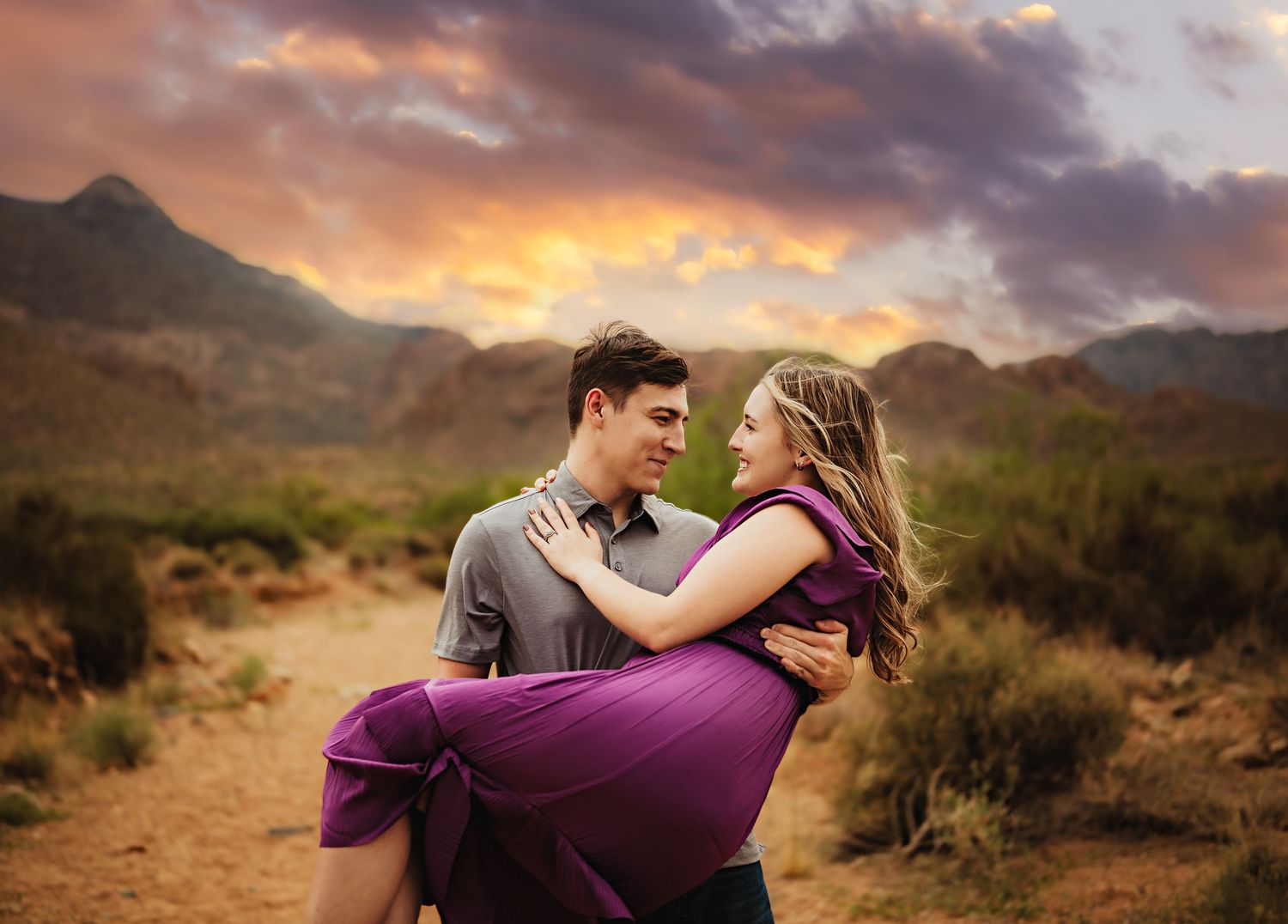 Romantic desert engagement photoshoot at sunset with dramatic clouds and mountain backdrop in Arizona.