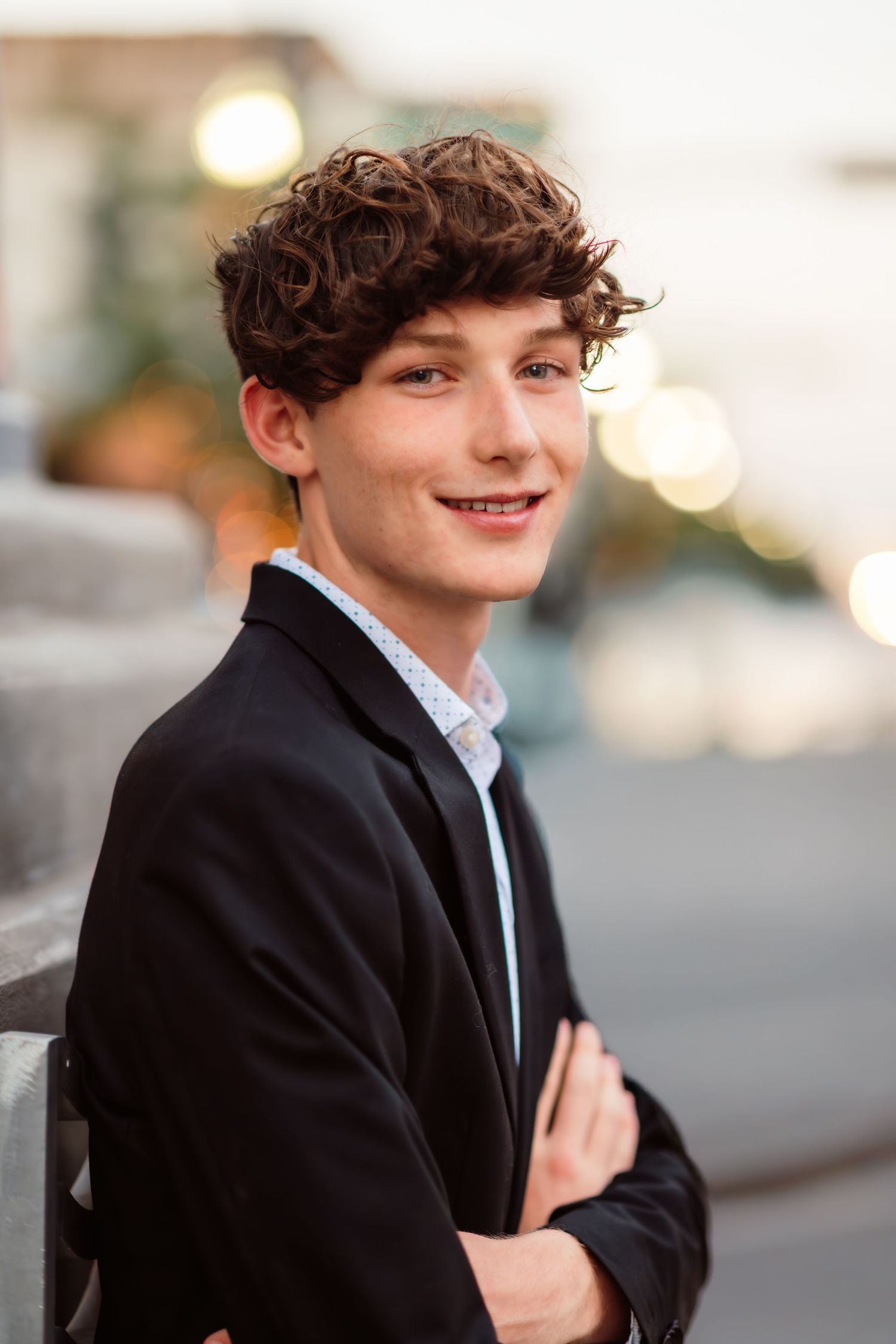Portrait of a young man in formal black suit and white shirt against blurred urban background.