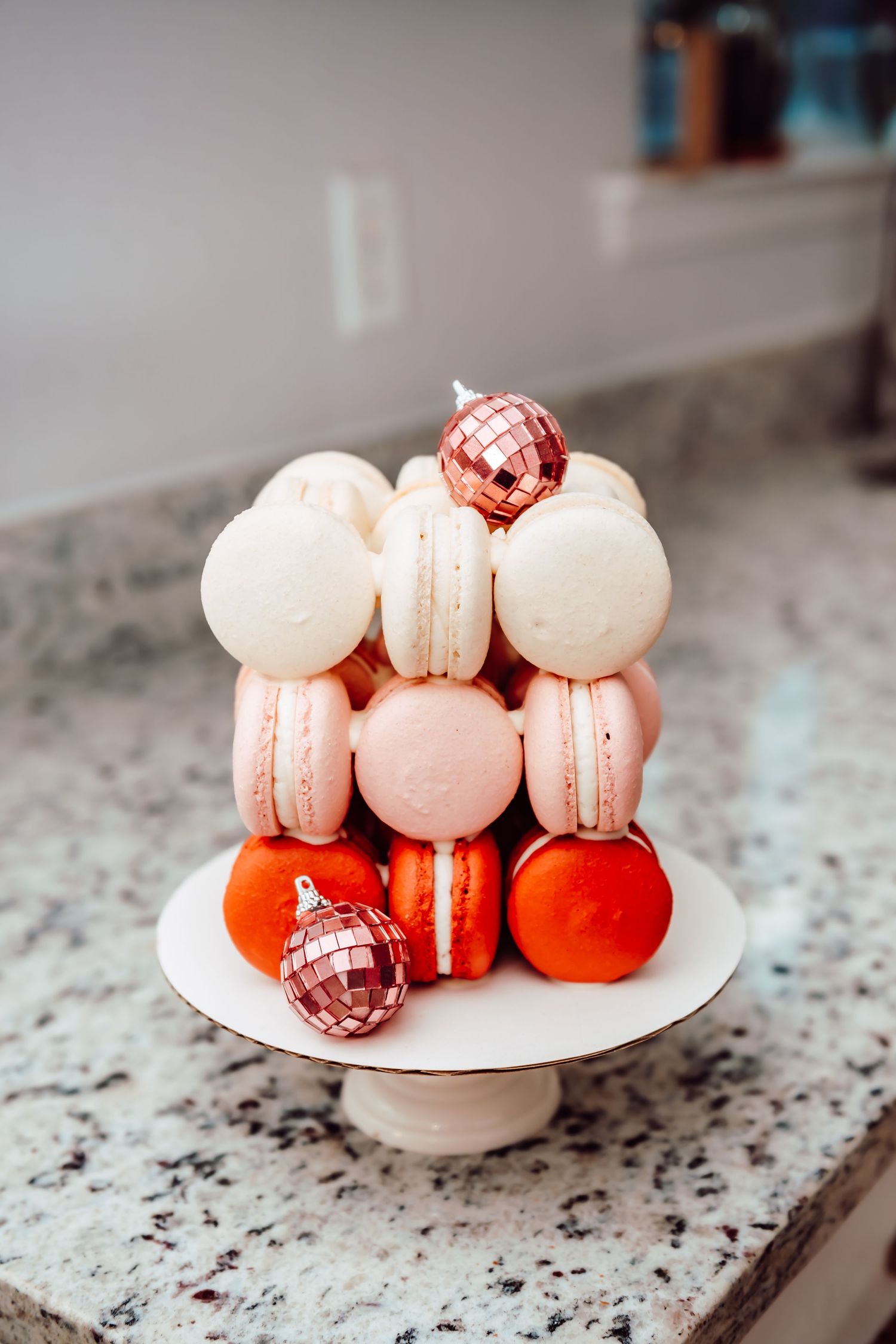 Pink and white macarons arranged with rose gold disco ball ornaments on a white plate against marble countertop.