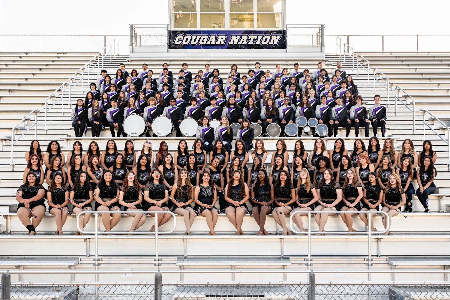 Cougar Nation marching band and dance team pose together in stadium bleachers for a group photo.
