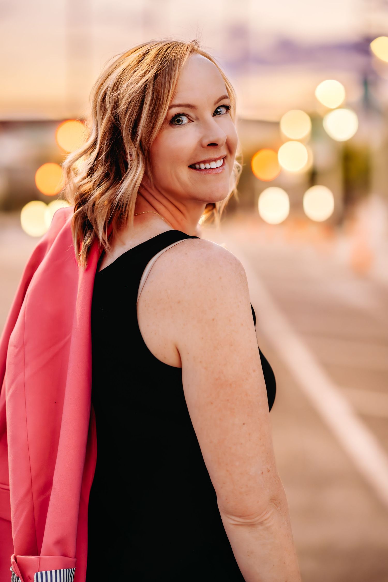 Elegant evening portrait session with pink jacket against blurred city lights.
