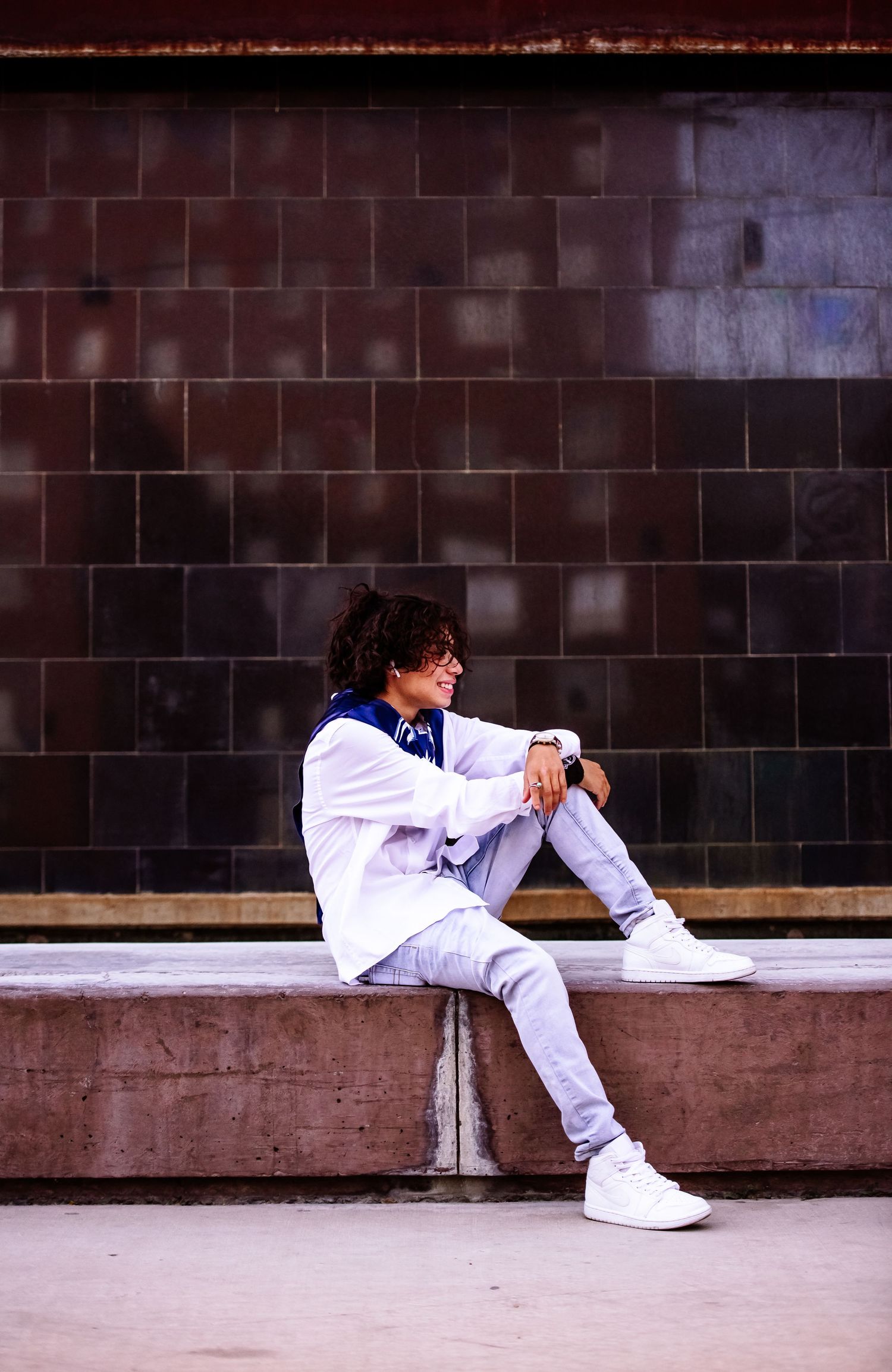 Person in white outfit and sneakers sitting against dark wall in four different relaxed poses.