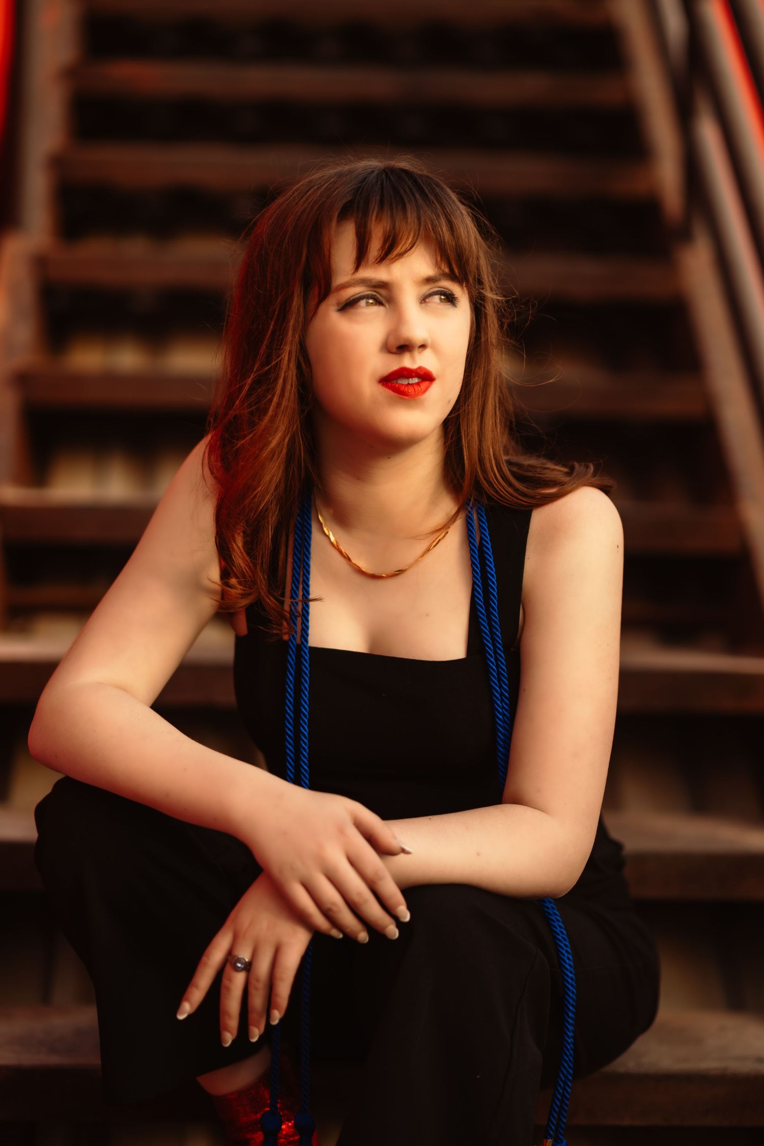 Dramatic portrait on wooden stairs wearing black dress with red lipstick.