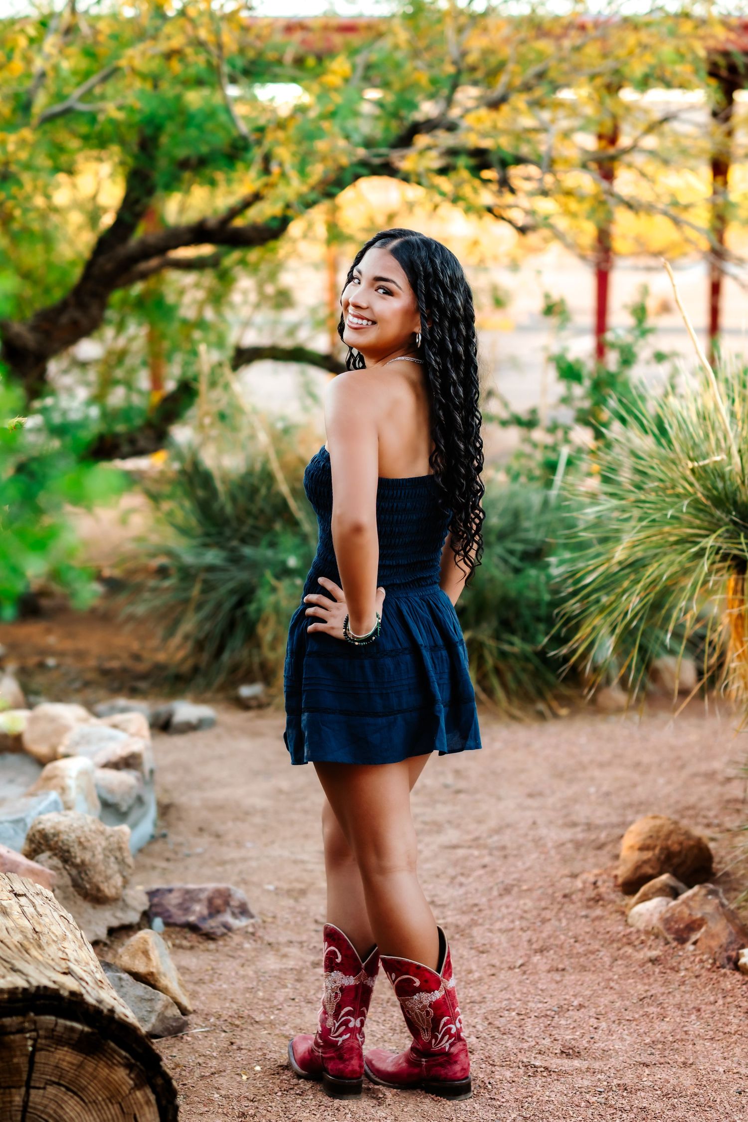 Woman in black dress and red boots poses on desert trail with natural landscape.