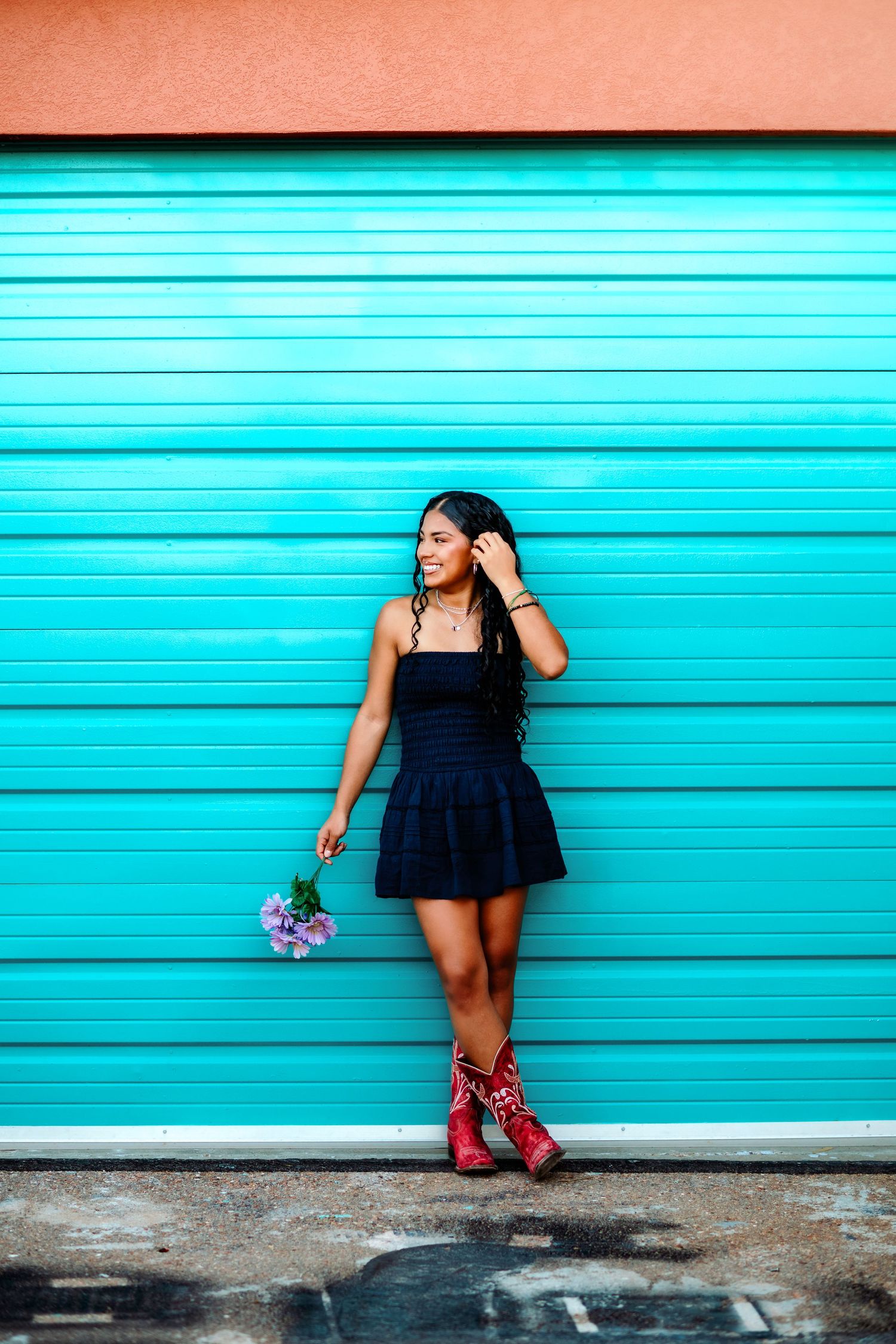 A woman in a navy dress poses playfully against a bright turquoise wall.