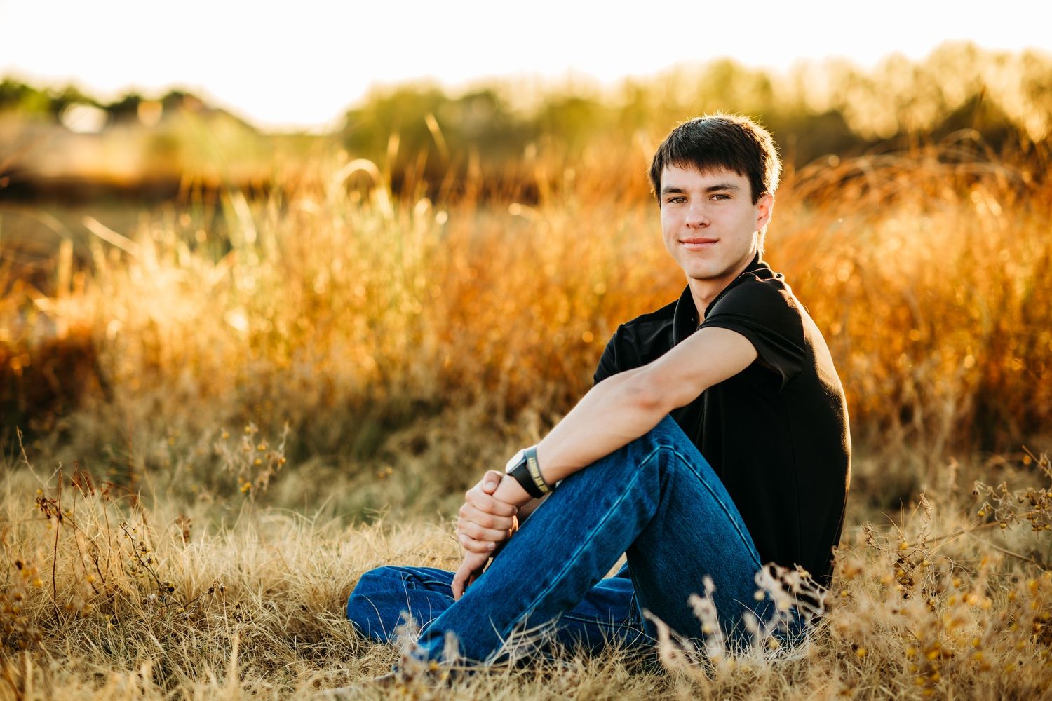 Student sits casually in golden field during sunset photoshoot.