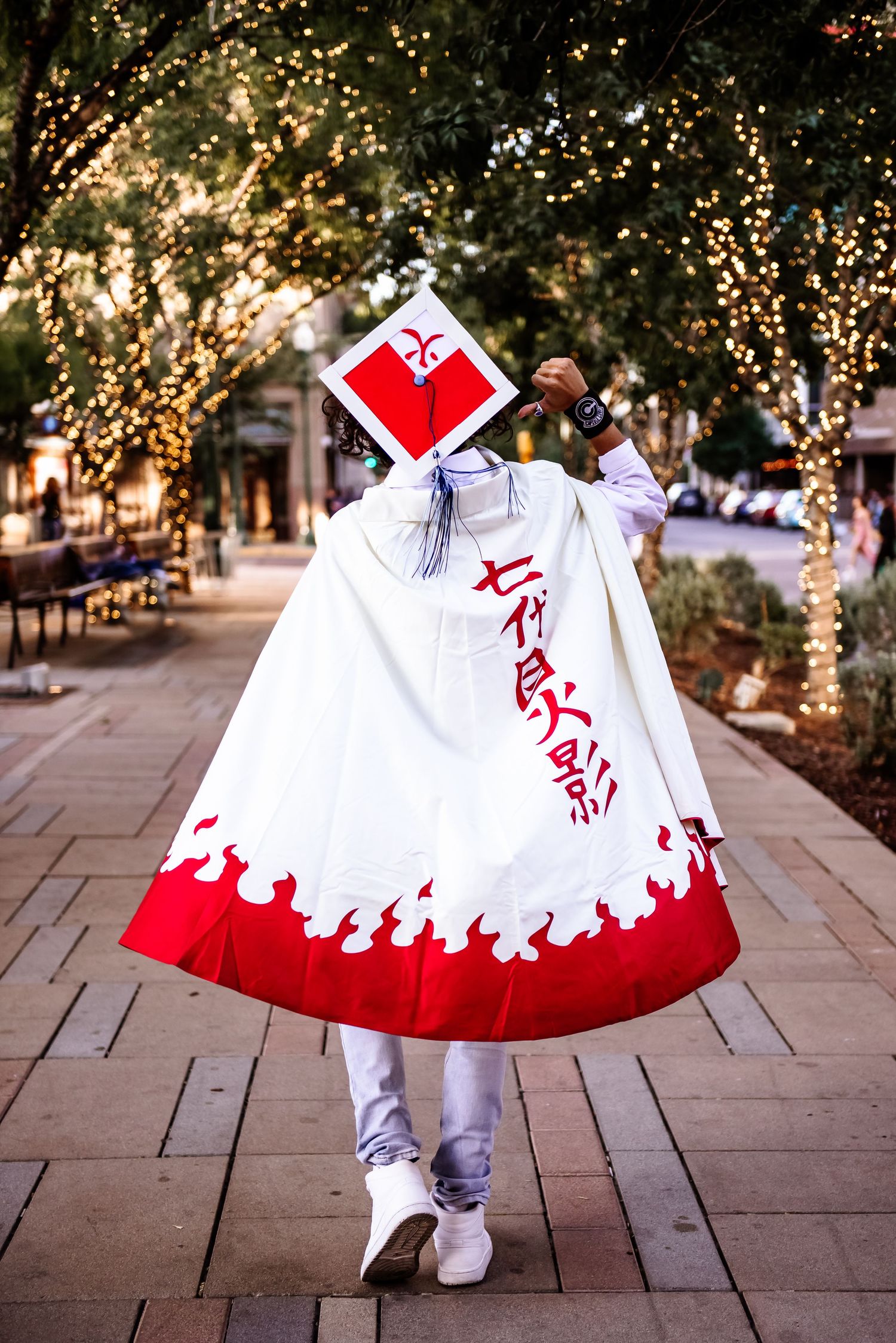A white dress with a red hem twirls on a stone pathway surrounded by trees and string lights.