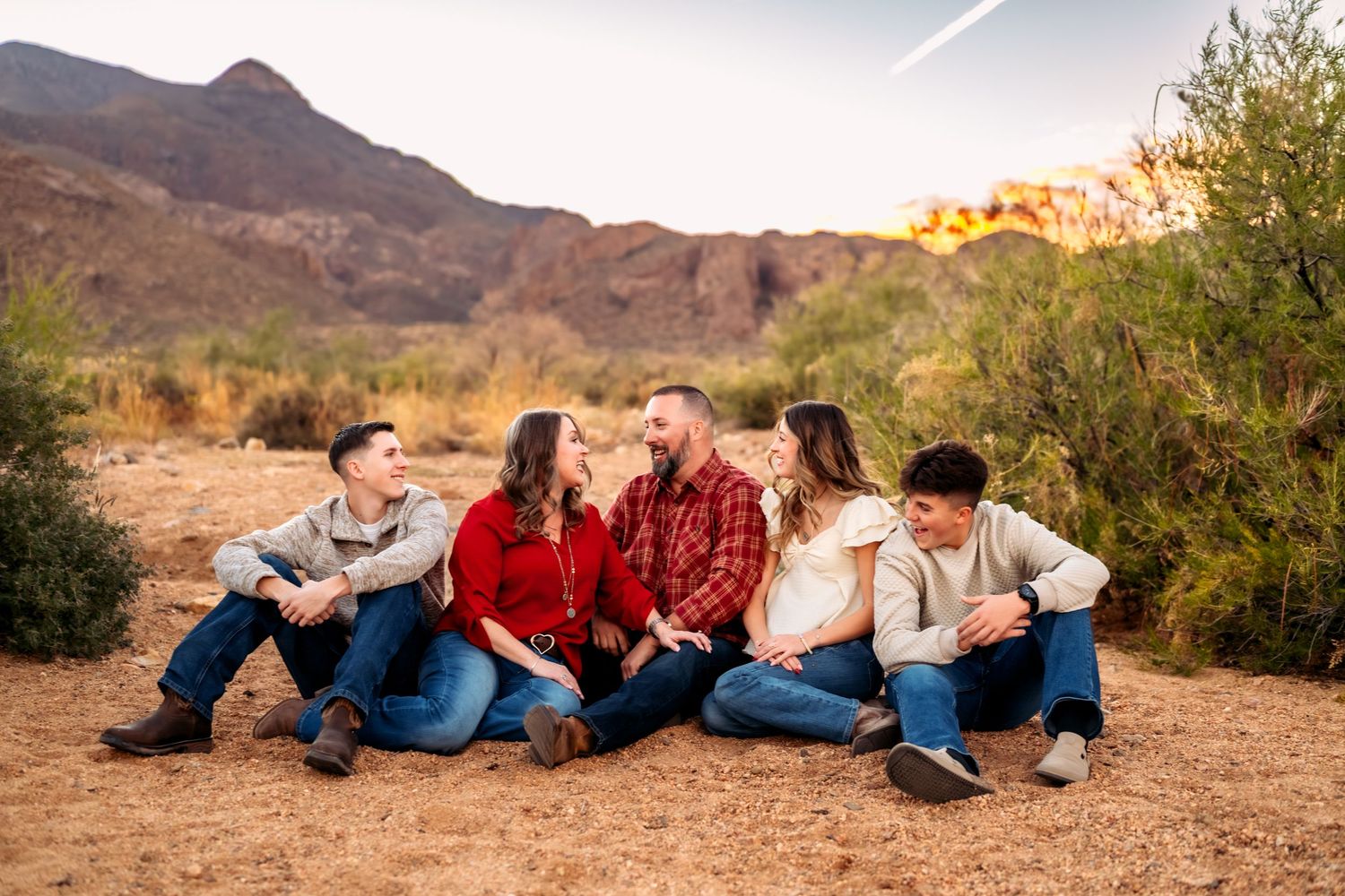 Family members lying down together on desert ground during sunset photo session.