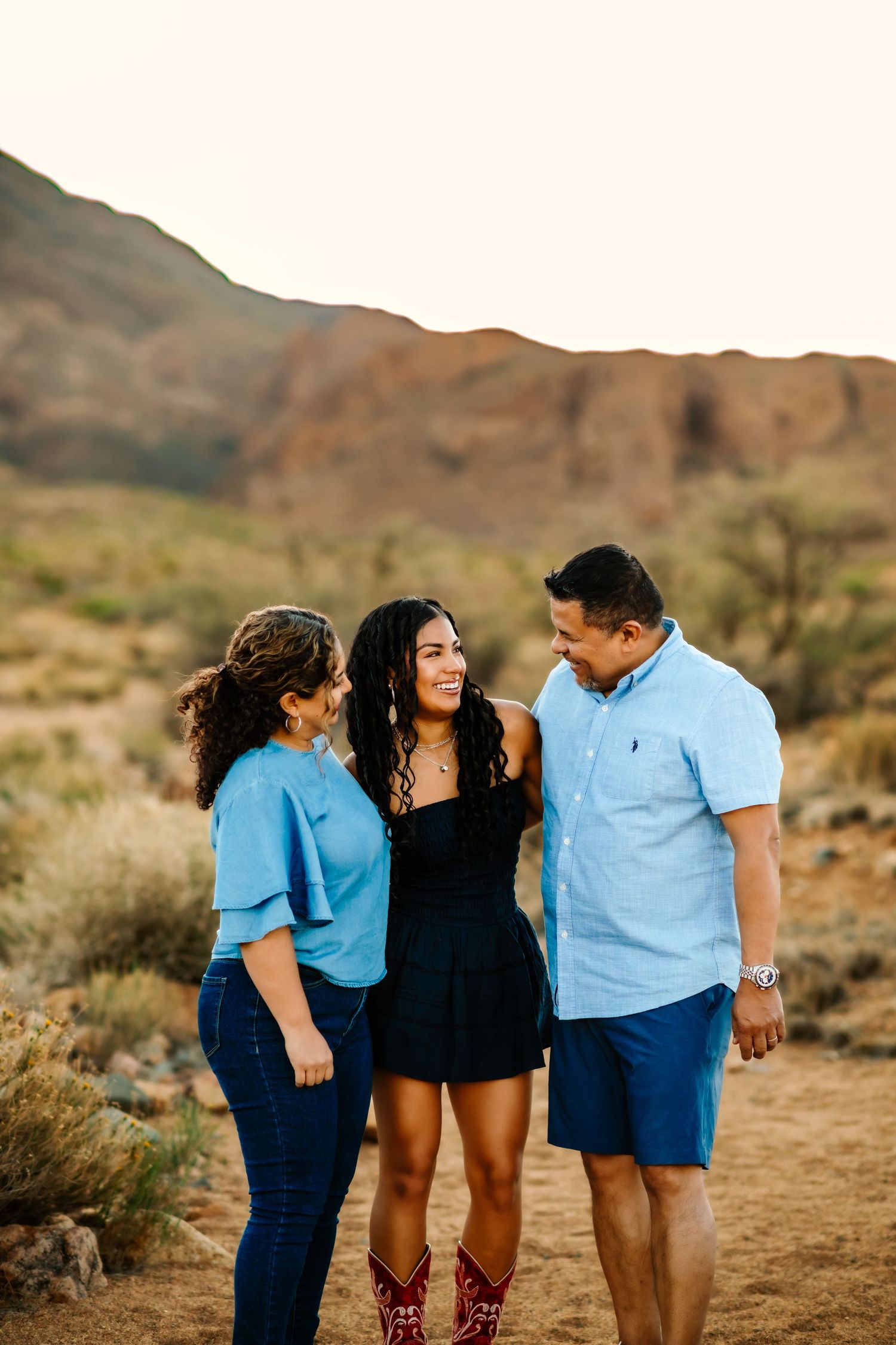 Three people share a warm moment together on desert trail during sunset.