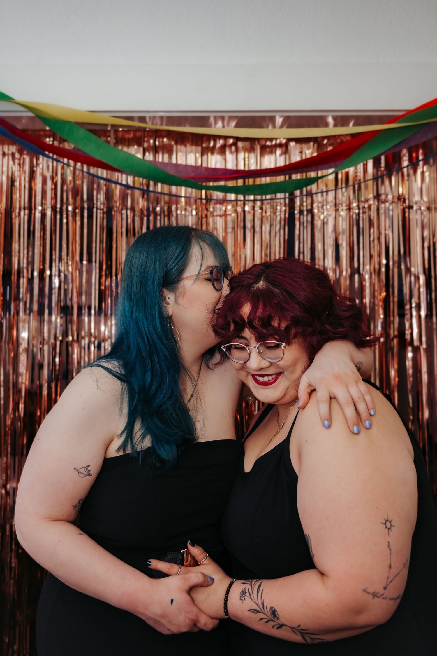 Two people share intimate moments in front of a sparkly rose gold backdrop with festive green garland decorations.