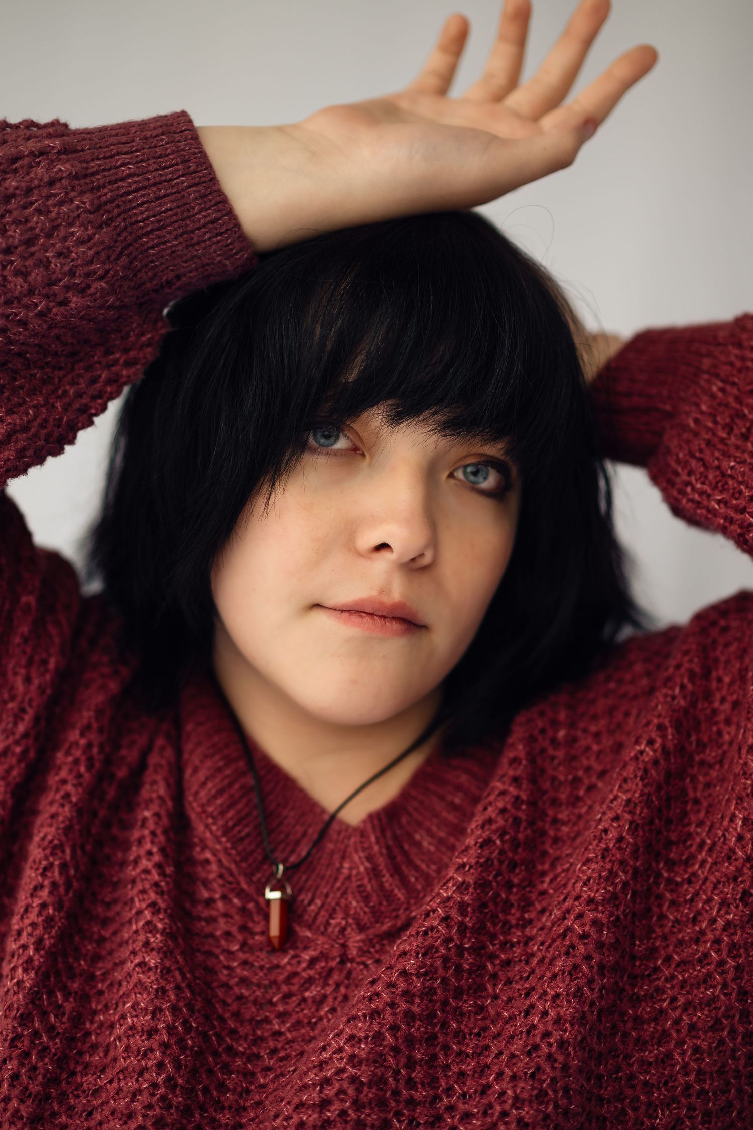Person wearing a burgundy knit sweater poses with hands raised against neutral background.