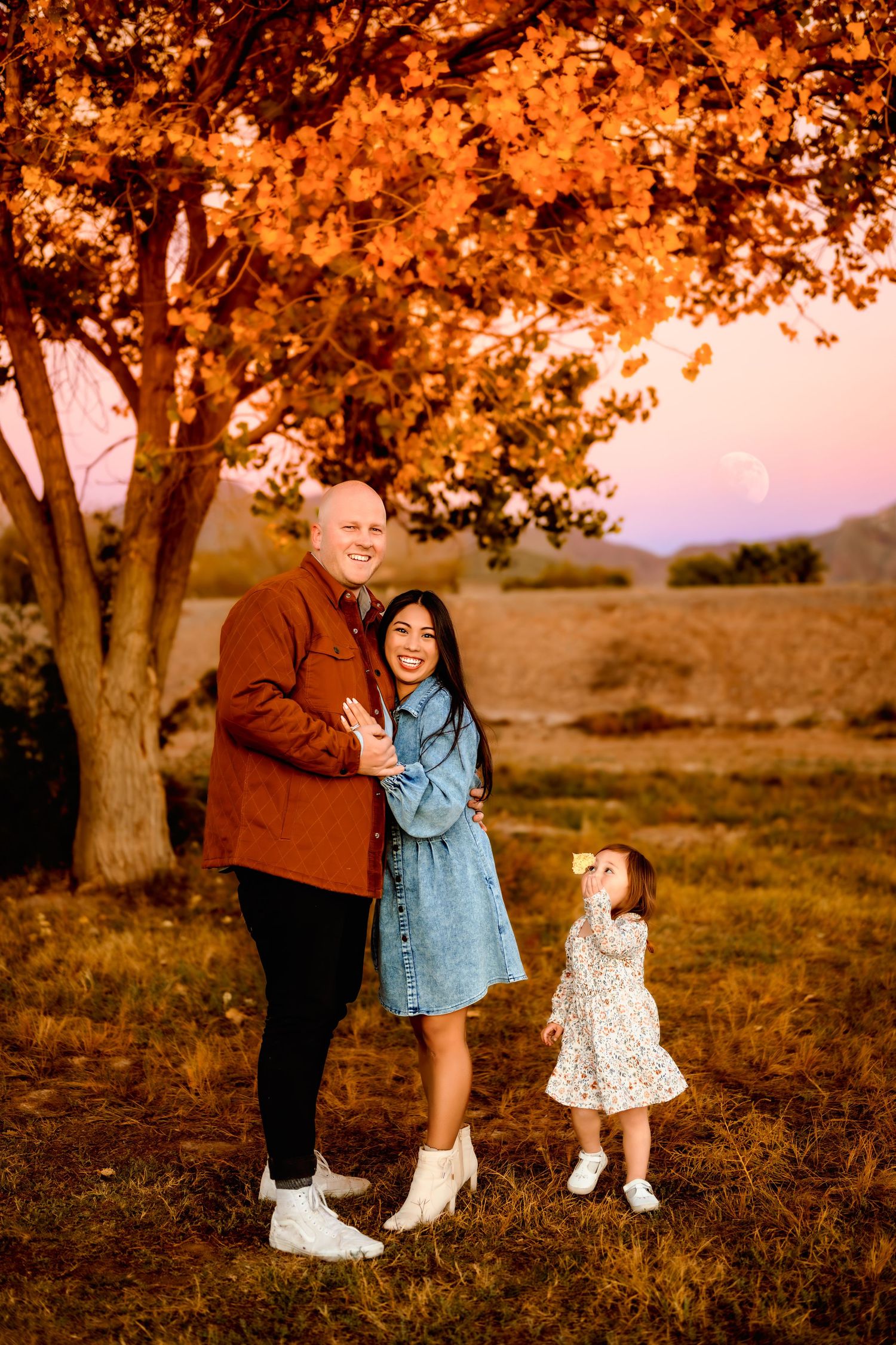 Autumn family photoshoot with golden leaves and warm sunset lighting in a rustic outdoor setting.