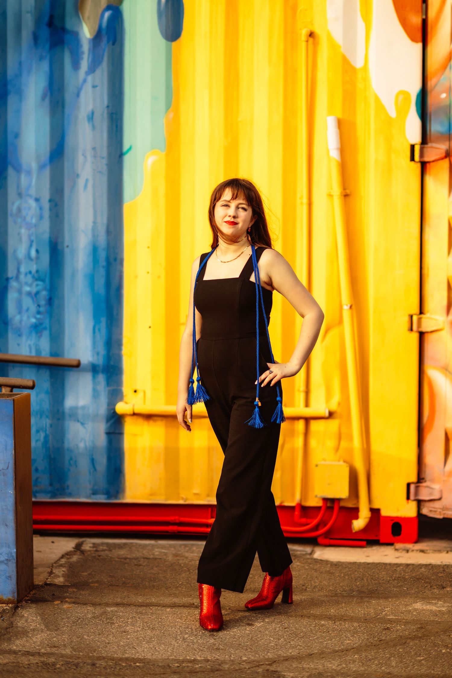 Stylish pose against vibrant yellow and blue industrial backdrop wearing black outfit.
